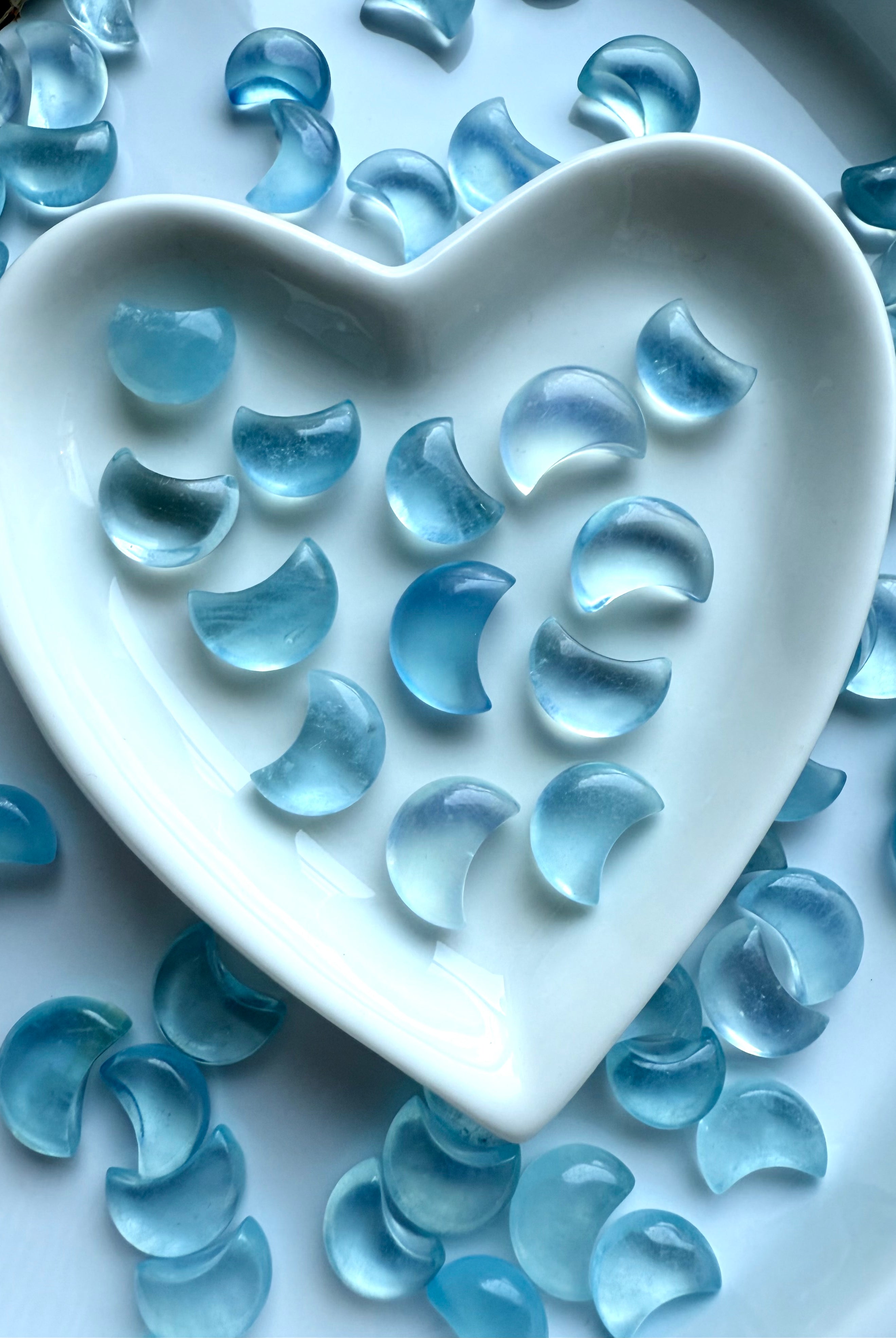 Closeup of Aquamarine moons inside a heart dish — deep ocean blue clarity and smooth polish captured in soft natural light