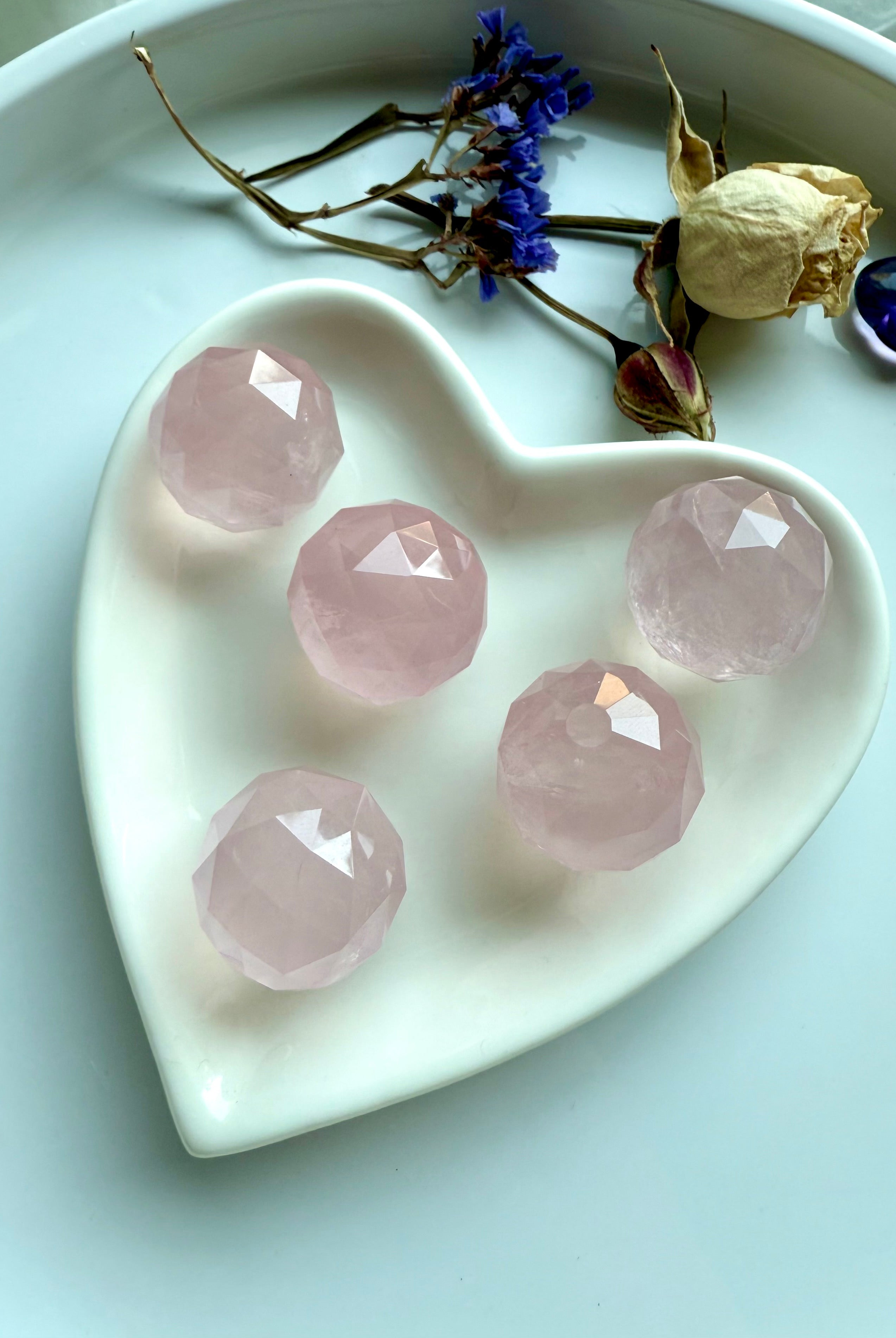 Faceted rose quartz crystal spheres inside a heart-shaped white dish. Soothing pink crystals for love.