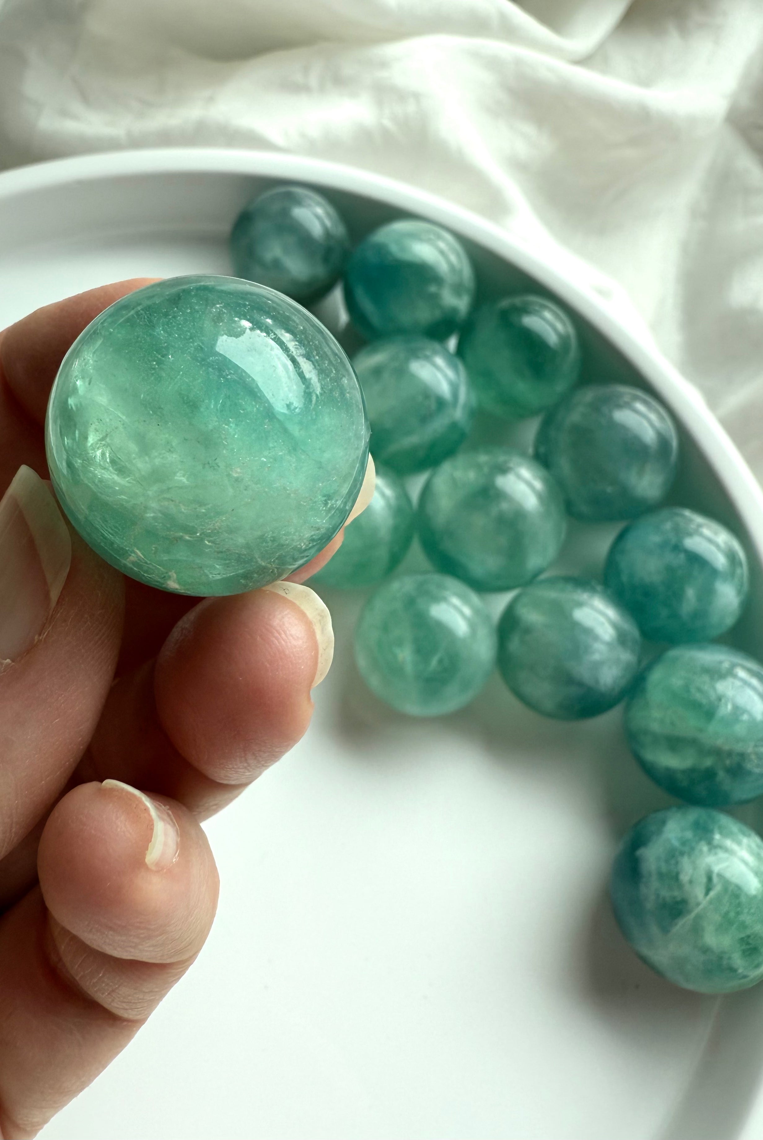 Hand holding a mini teal Fluorite sphere with shimmering aqua tones for clarity, calm, and focus.