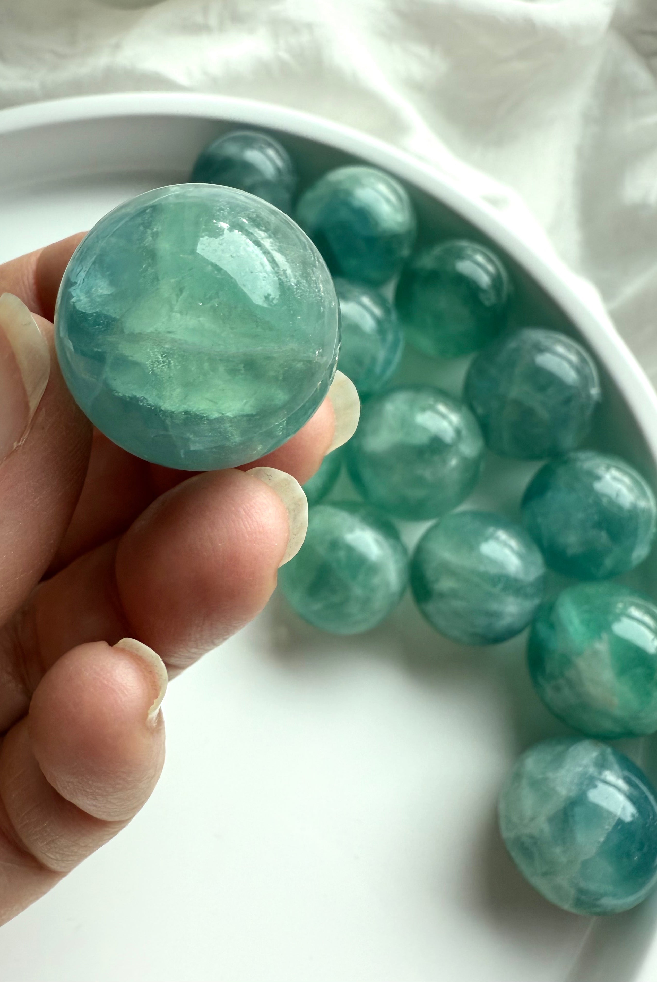 Hand holding a polished teal Fluorite crystal ball showing translucent blue-green patterns for meditation and chakra healing.