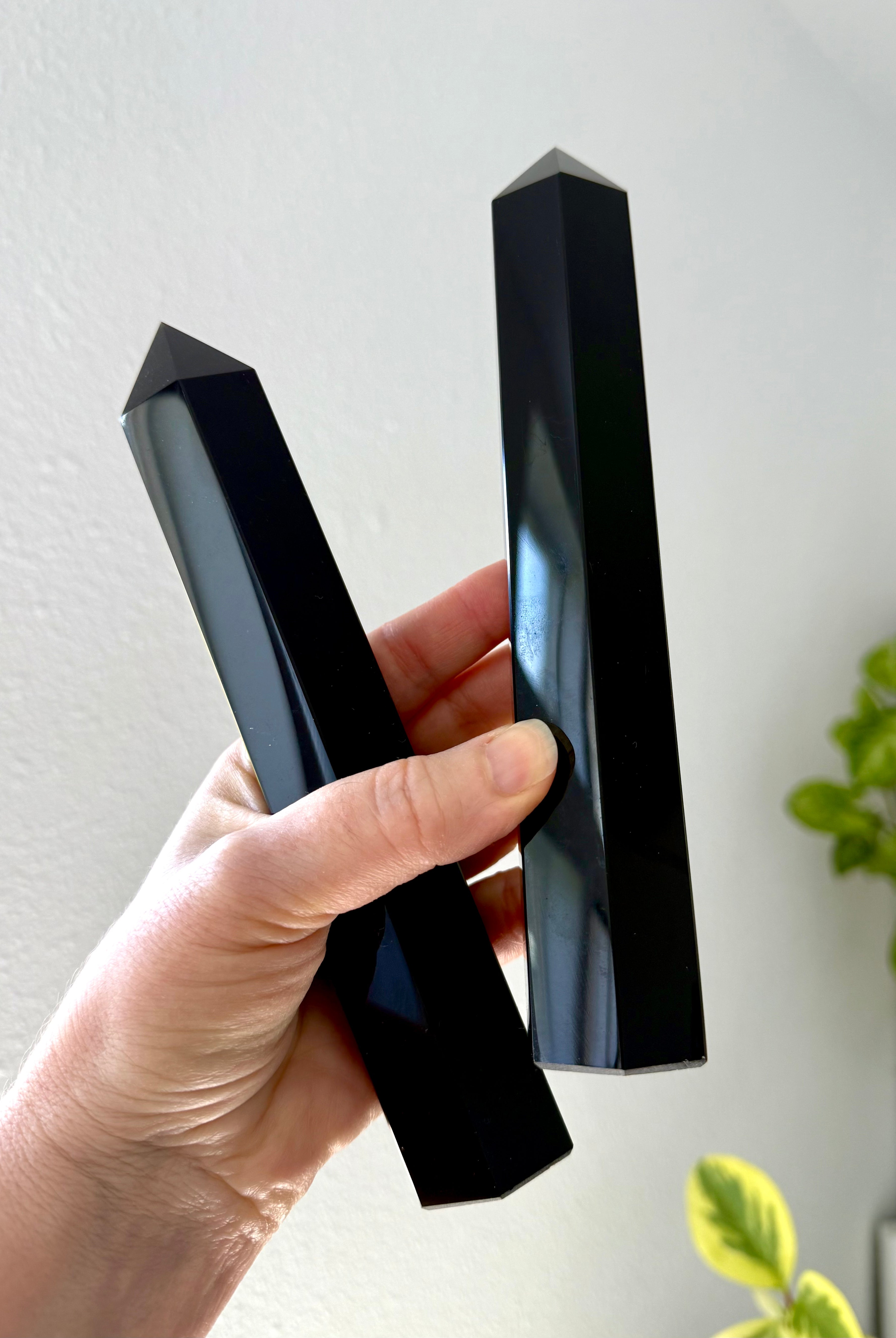 Hand holding two large Black Obsidian towers at an angle — glossy polished crystals for energetic protection & grounding.