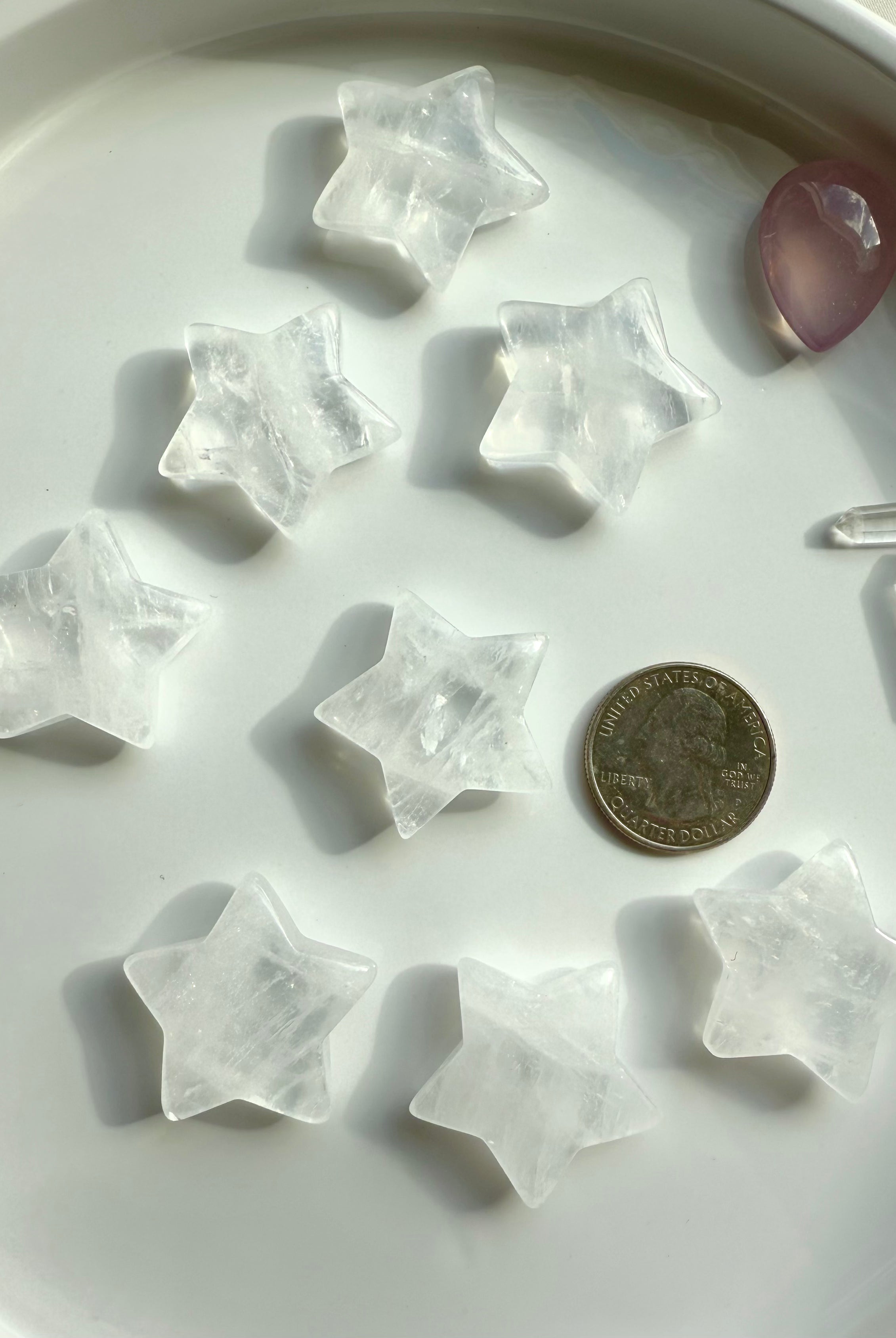 Clear Quartz star carvings on white plate with quarter for size reference, small healing crystals for chakra balancing and grids
