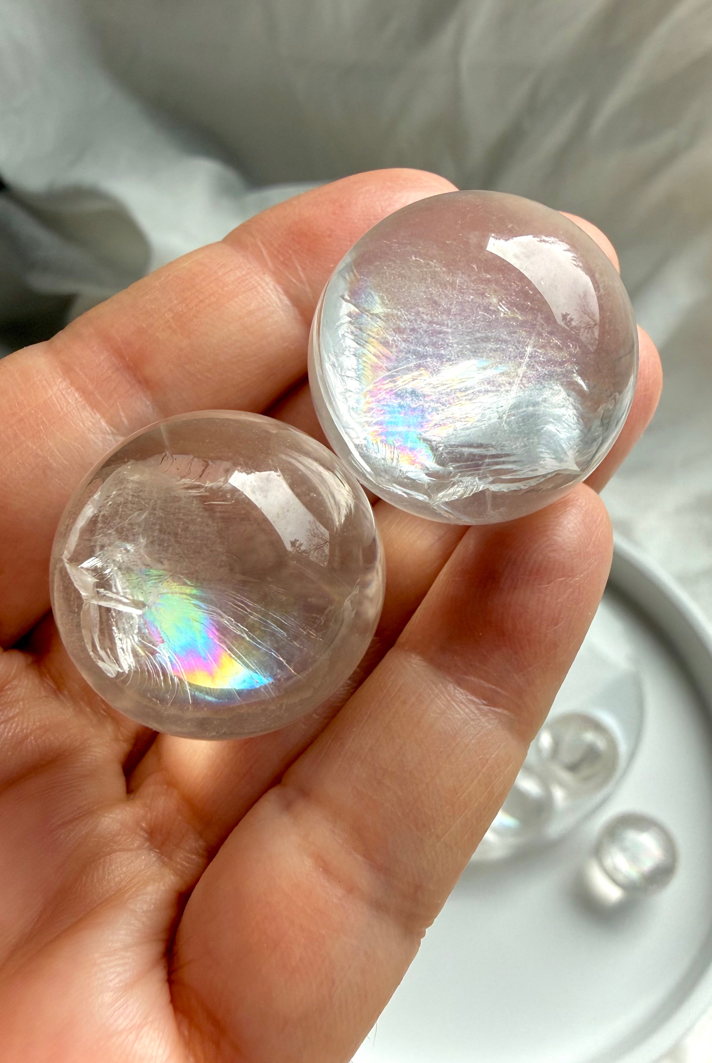Hand holding two rainbow girasol mini quartz spheres, milky crystal ball with soft ethereal glow and natural rainbow inclusions