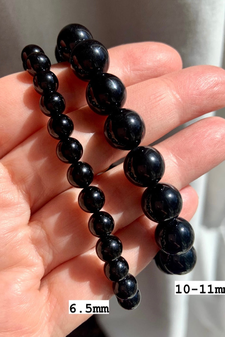 Two Black Tourmaline bracelets on hand marked 6.5mm and 10–11mm bead sizes — ideal for showcasing sizing and crystal bead quality