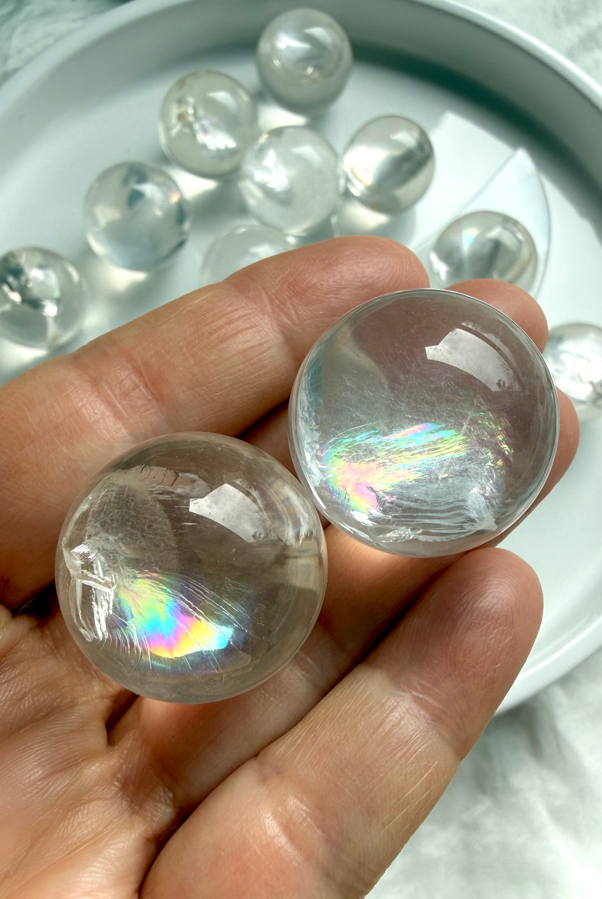Close-up of two rainbow girasol mini quartz spheres in hand, milky crystal balls with luminous opaline glow and subtle silvery rainbows