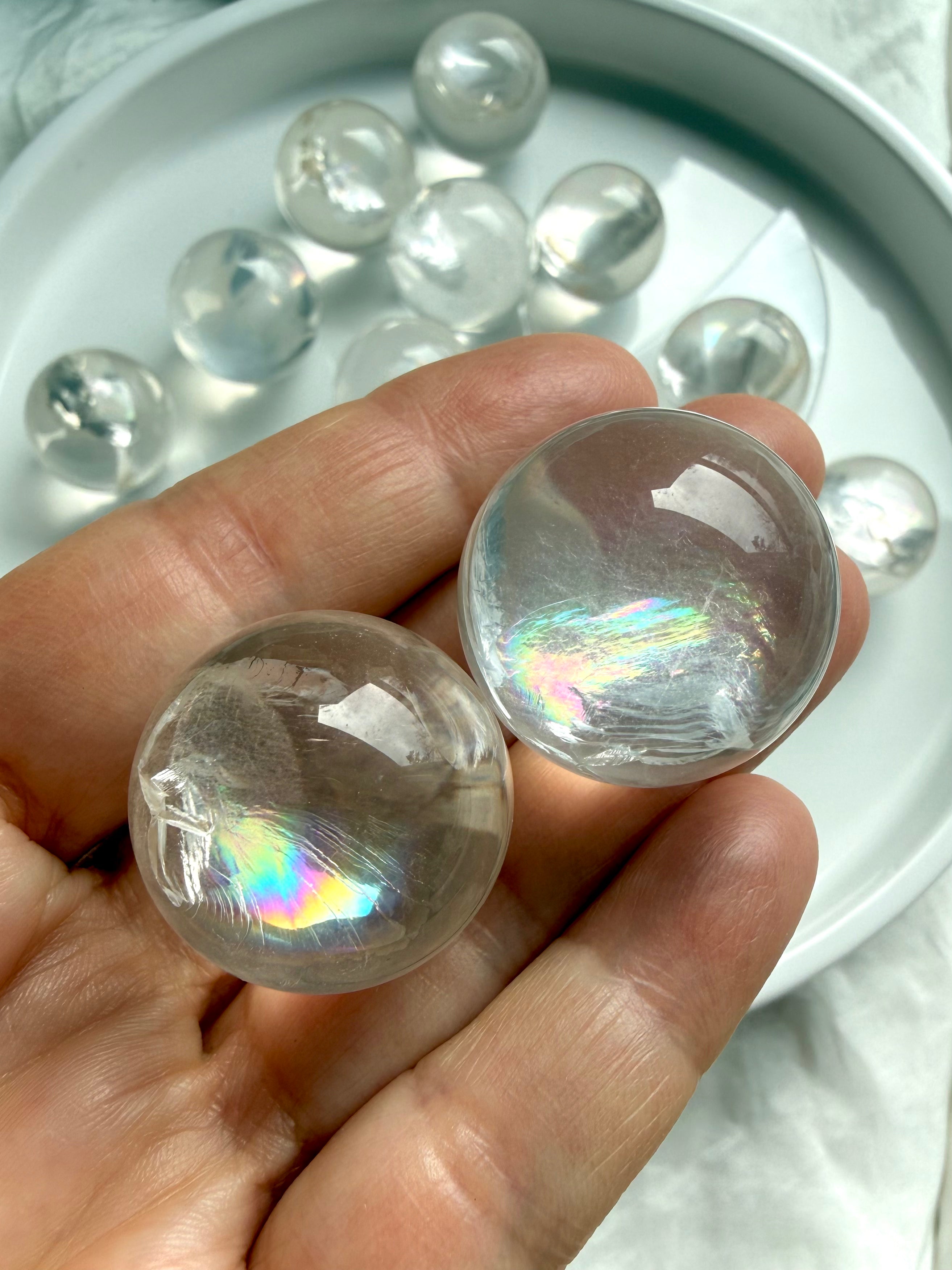 Close-up of two rainbow girasol mini quartz spheres in hand, milky crystal balls with luminous opaline glow and subtle silvery rainbows