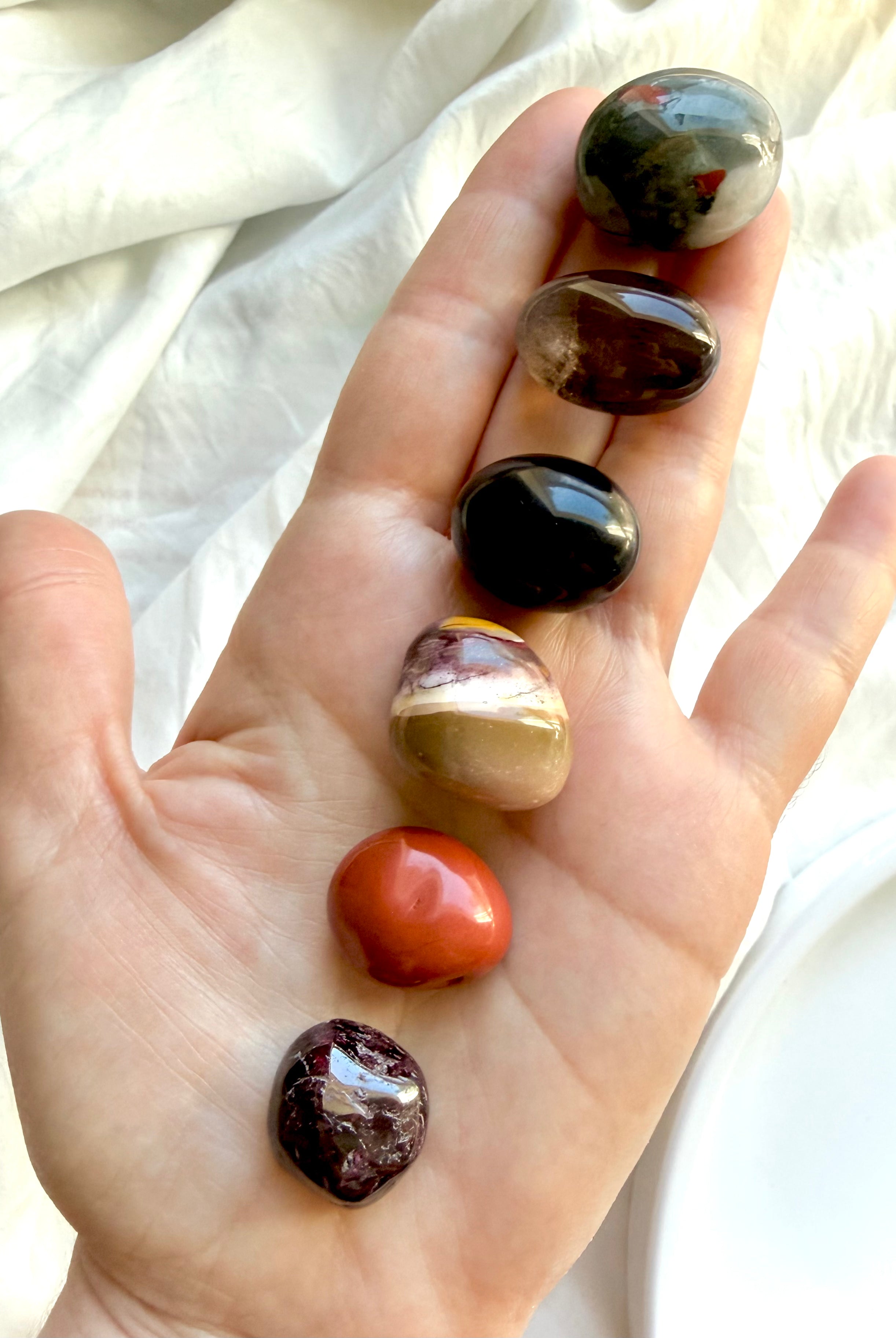 Hand holding a Root Chakra Crystal Set with Bloodstone, Black Obsidian, Red Jasper, Smoky Quartz, Garnet, and Mookaite Jasper