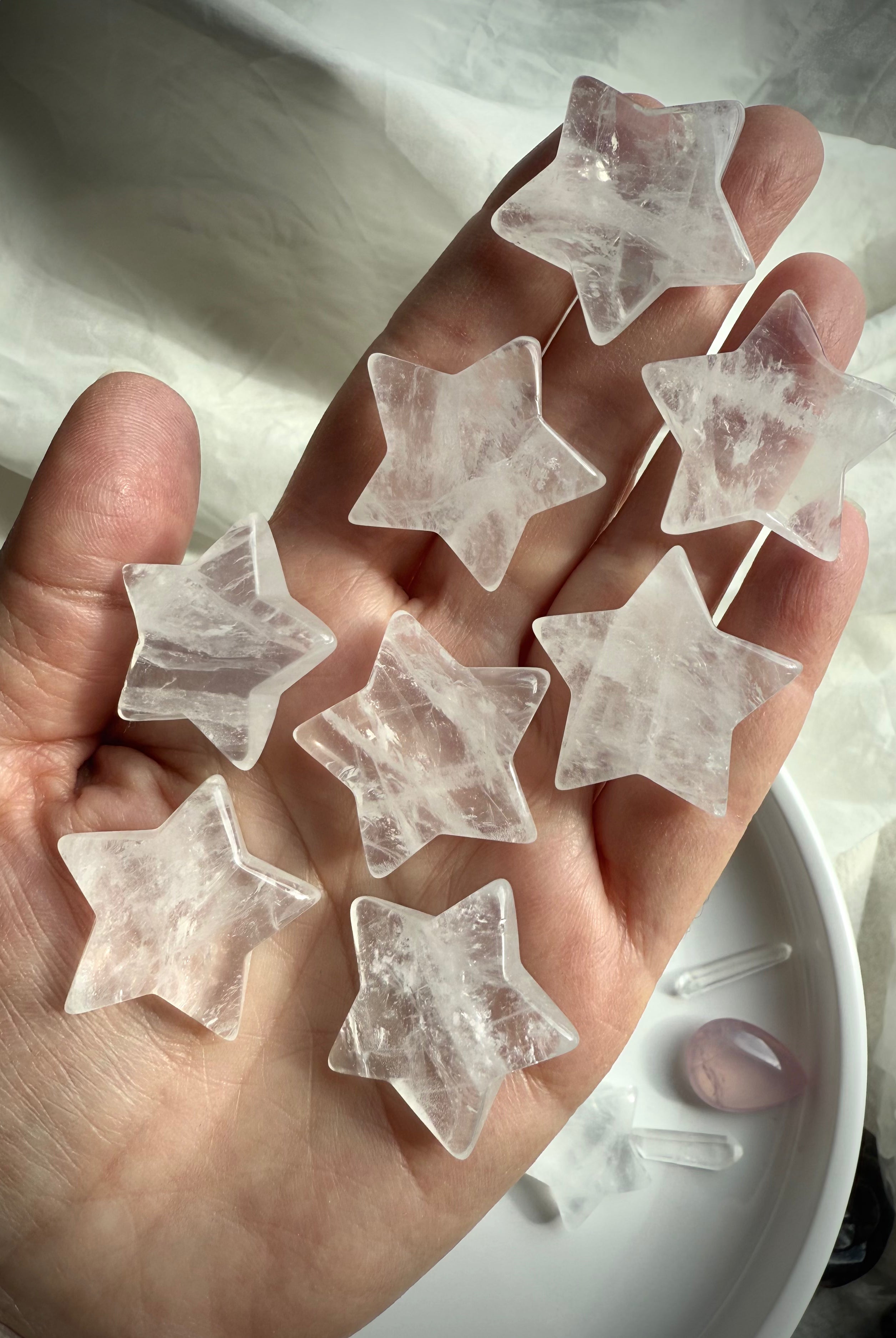 Clear Quartz stars displayed on hand over white silk, luminous crystal carvings for clarity and chakra healing
