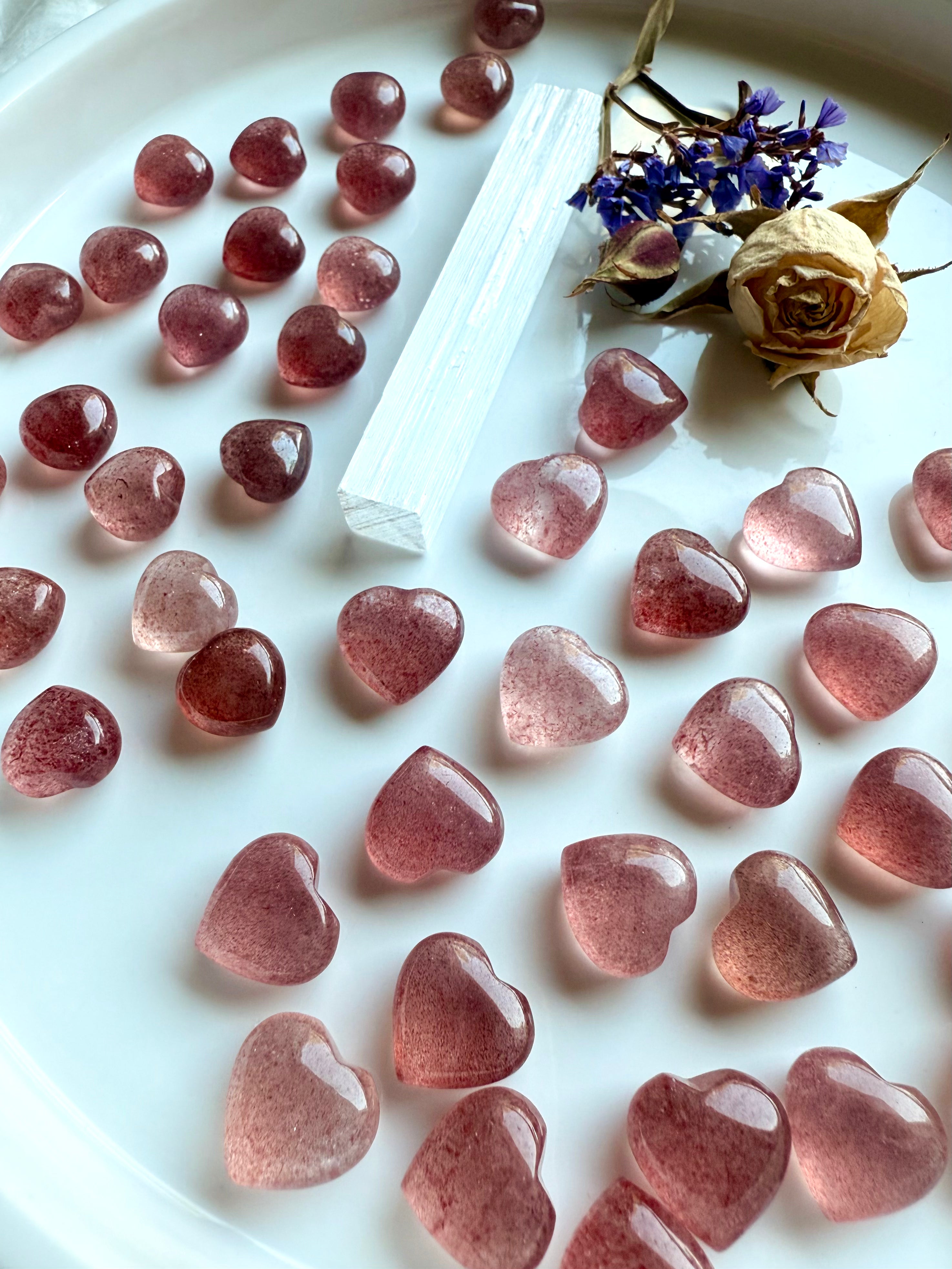 Angled view of Strawberry Quartz mini hearts arranged on a white with selenite & roses — pocket-sized tanzberry quartz carvings.