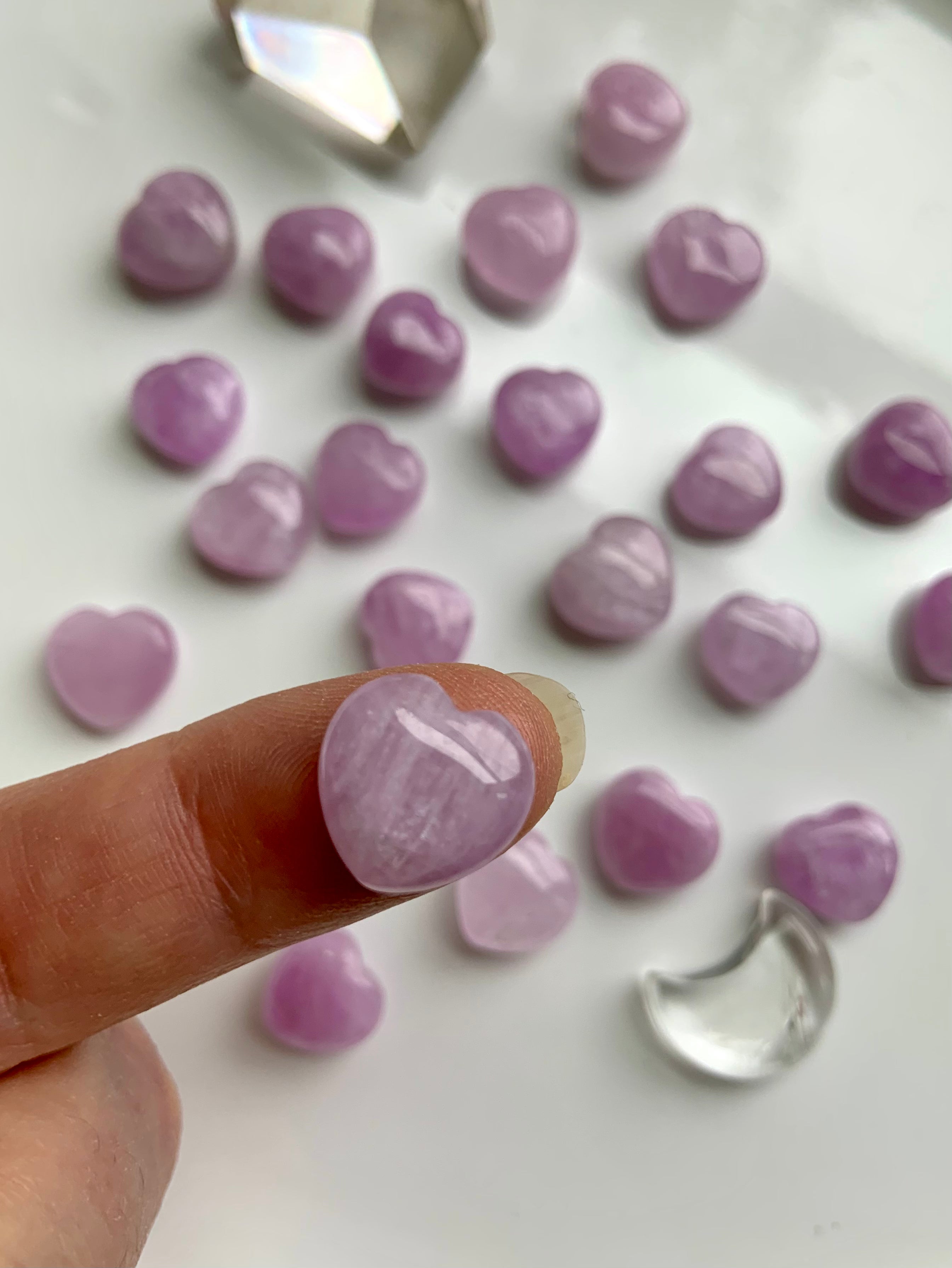 Mini Pink Kunzite heart shown on a fingertip for scale with more hearts in the background β tiny crystal carving for emotional healing & crystal gifting.