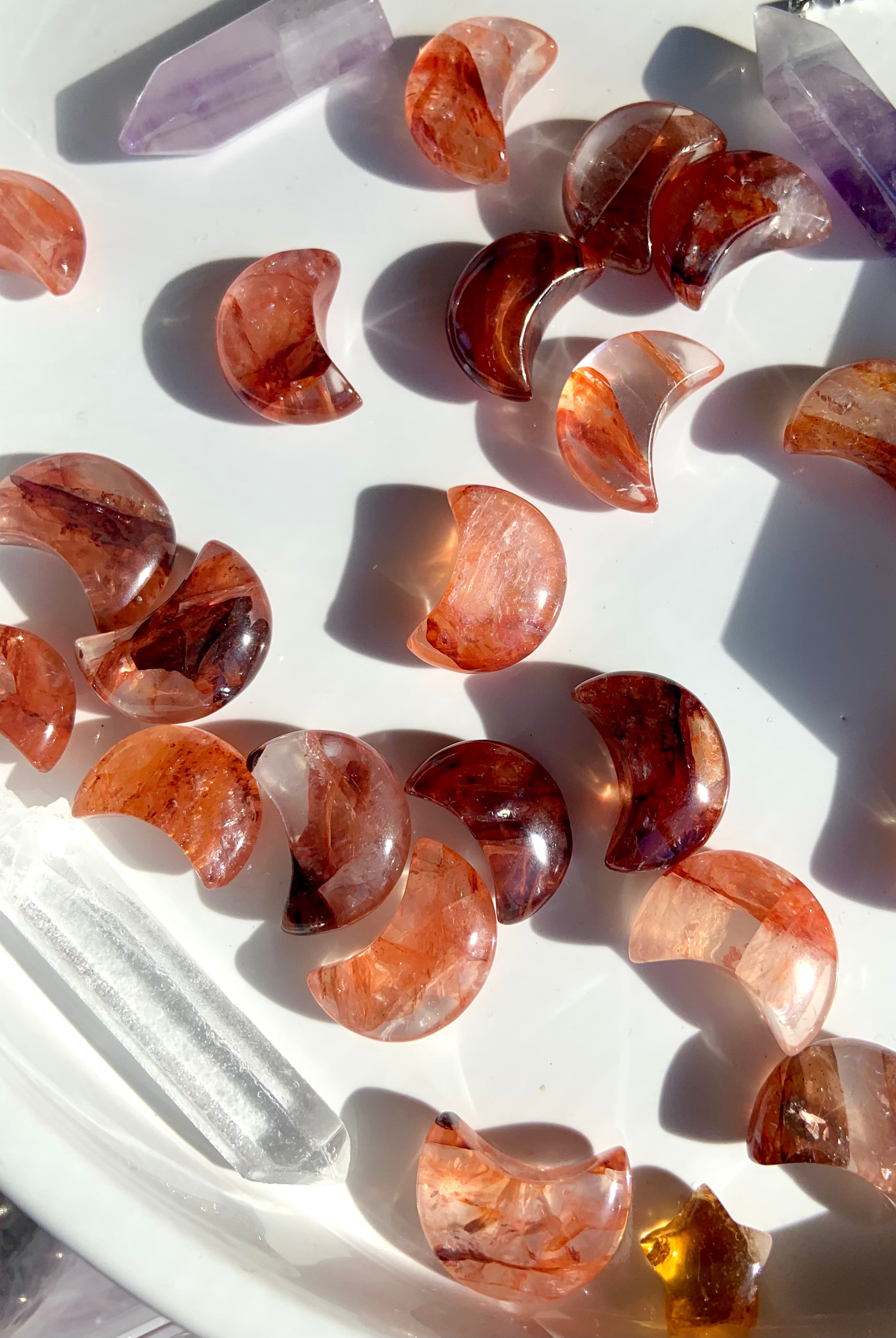 An array of vibrantly colored mini sized fire quartz crescent moons on a white plate with some other crystals