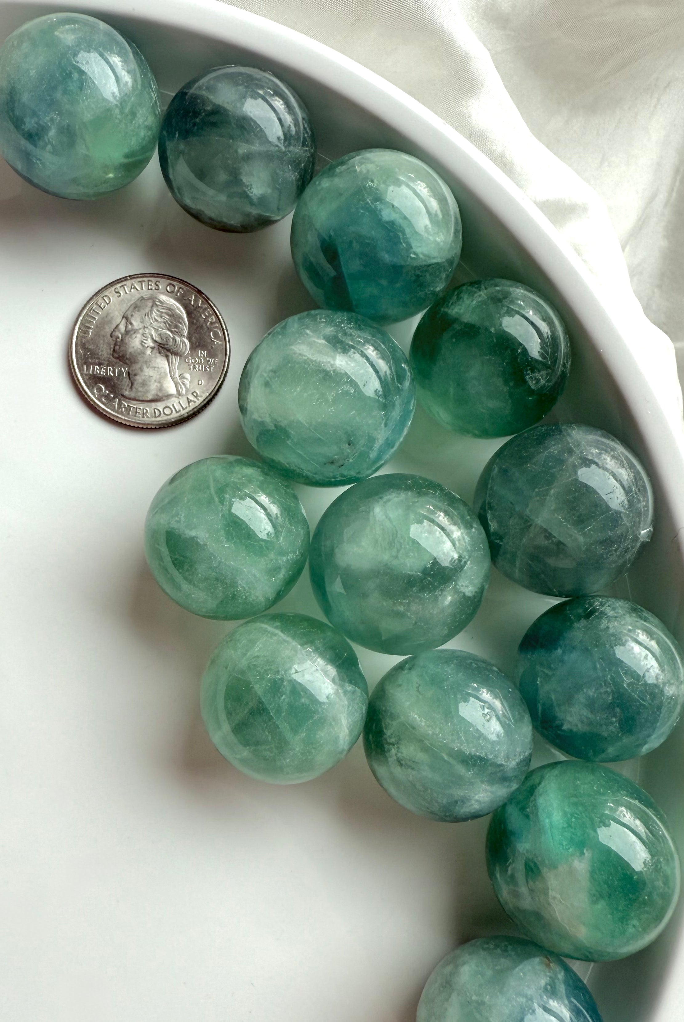 Mini teal Fluorite crystal spheres with aqua tones next to a U.S. quarter for size comparison.