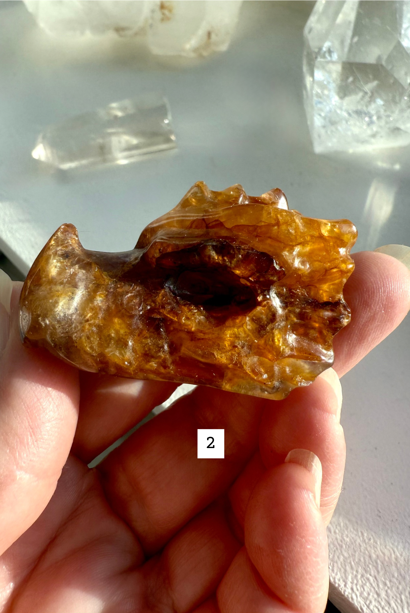 Hand holding Golden Healer Quartz dragon head with hematite inclusions and golden light patterns — crystal carving for chakra alignment and energy healing.