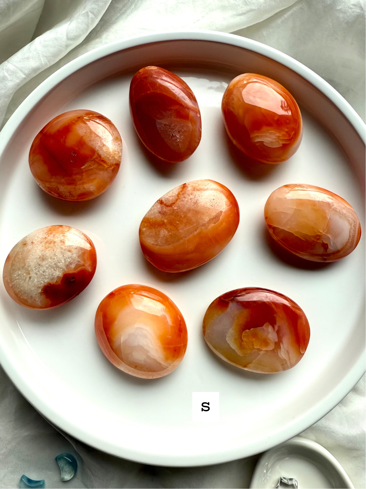 Polished small Carnelian palm stones on a white dish labeled size S — orange and red banded agate crystals for vitality, motivation + Sacral Chakra healing.