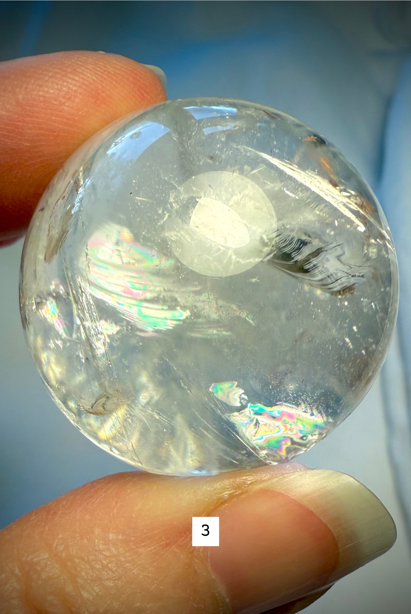 Hand holding Rainbow Quartz sphere #3, highlighting brilliant internal rainbows and natural inclusions.