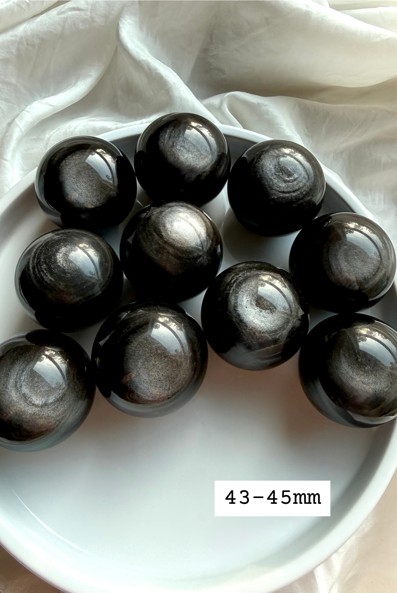 Silver Sheen Obsidian crystal spheres size 43-45mm on white tray, polished obsidian balls with luminous silver flash for protection and spiritual grounding