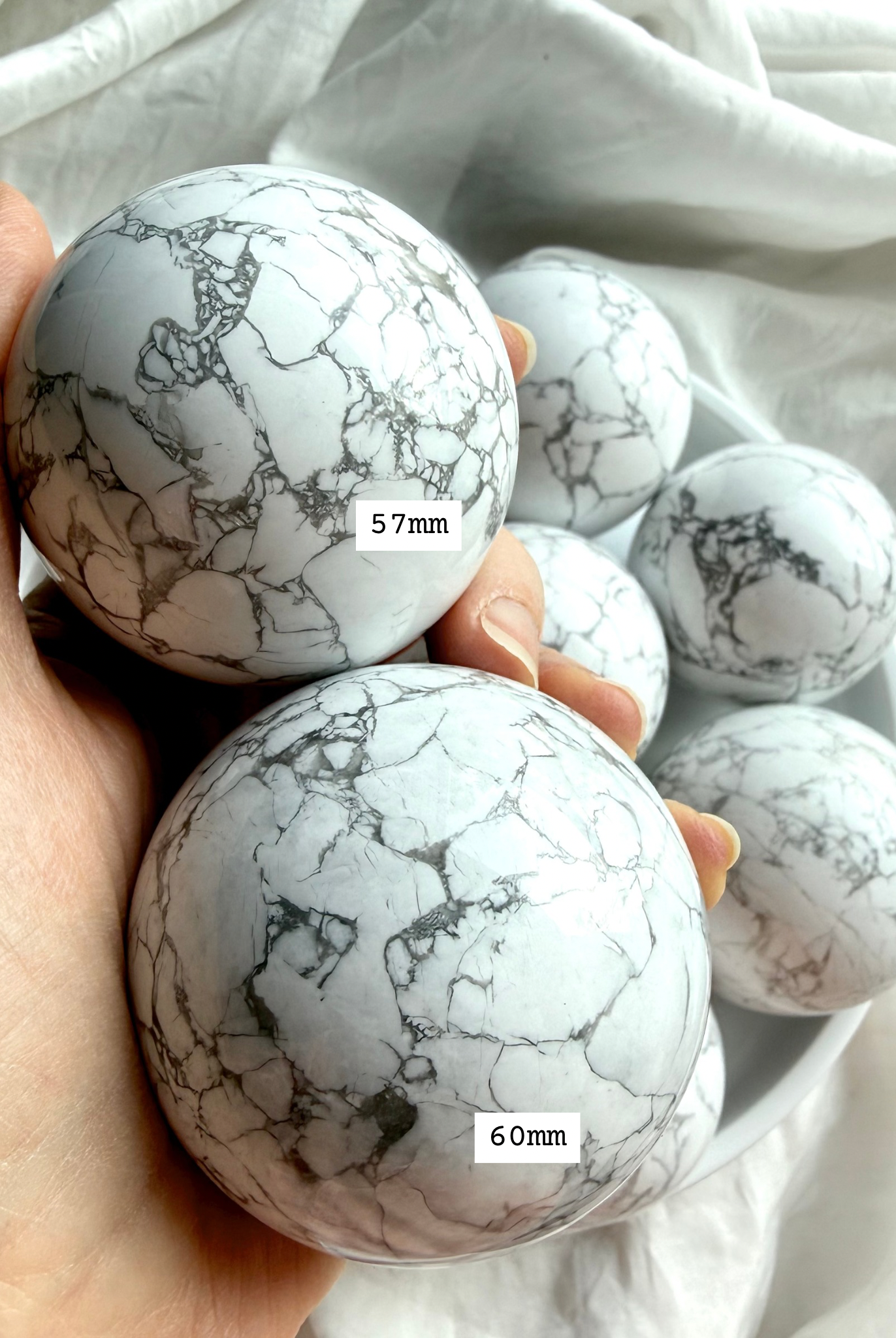 Howlite crystal spheres 57mm and 60mm shown in hand for size reference, polished white stone with gray marbling for calm and stress relief