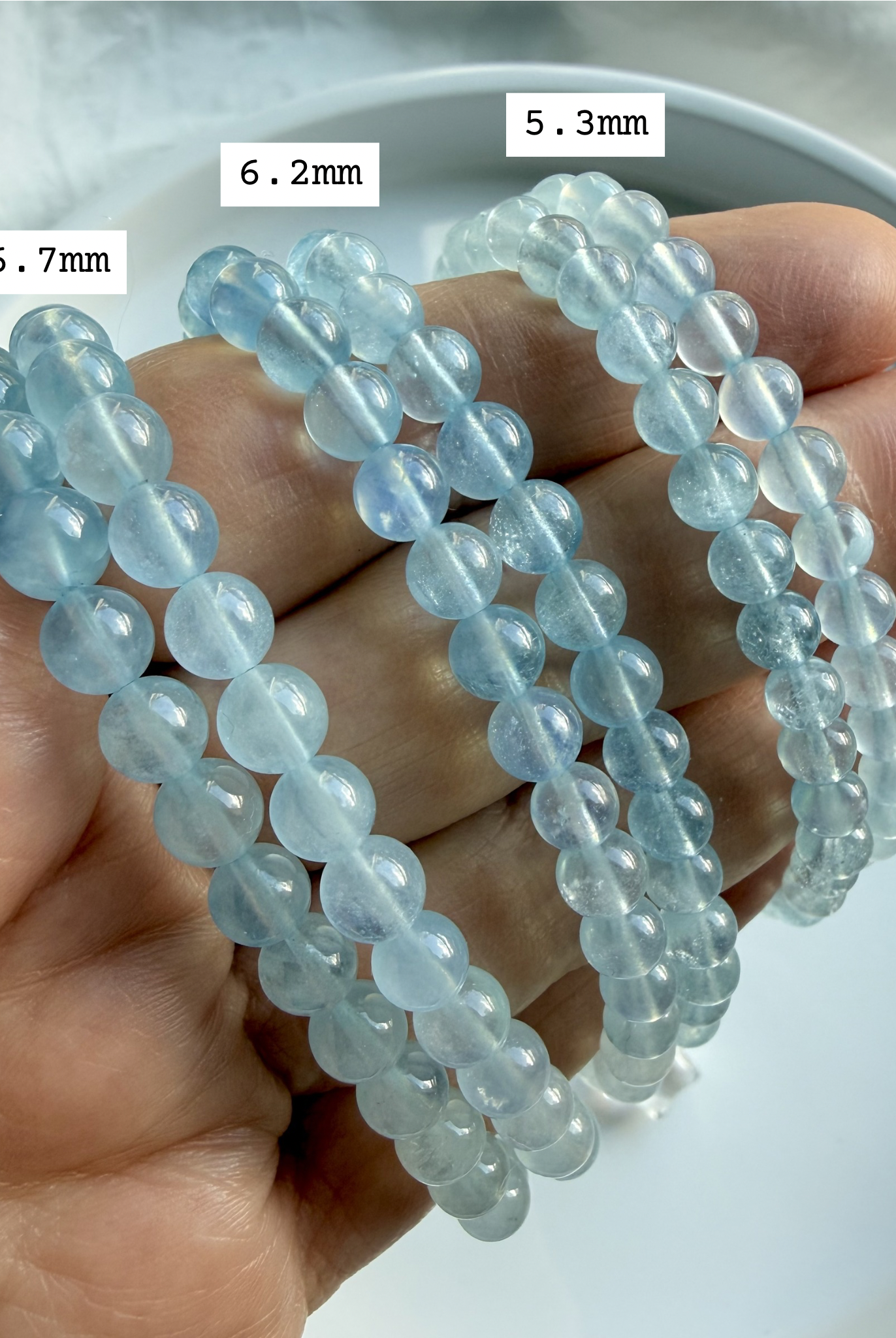 Aquamarine bracelets shown on hand in soft blue ombré – marked with bead sizes for comparison