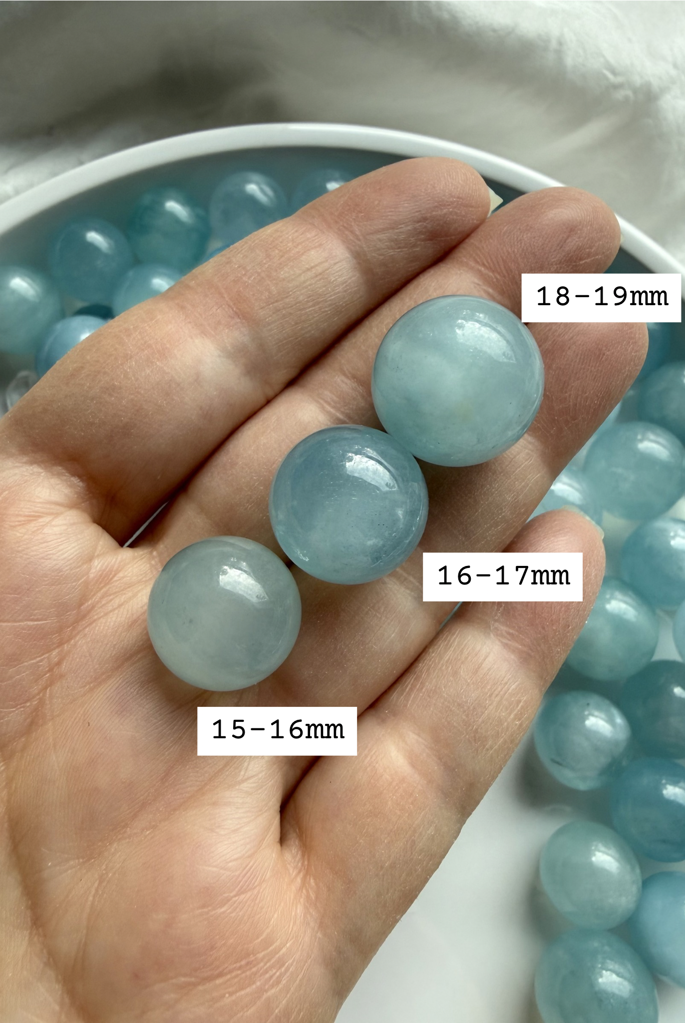 Mini Aquamarine crystal spheres with size labels held in hand – calming blue March birthstone stone