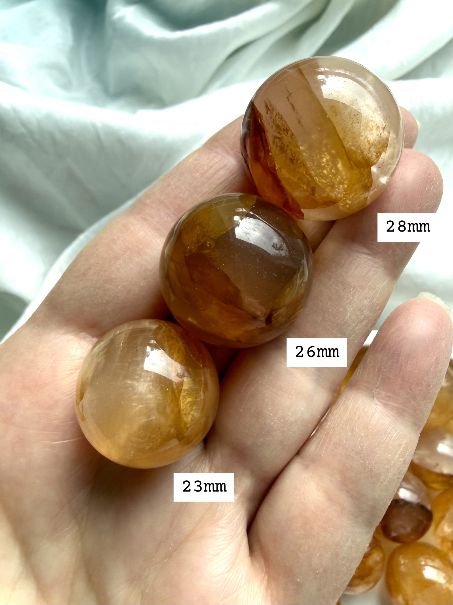 golden healer quartz mini spheres in hand with size reference showing 23, 26, and 28 mm diameter with natural golden inclusions