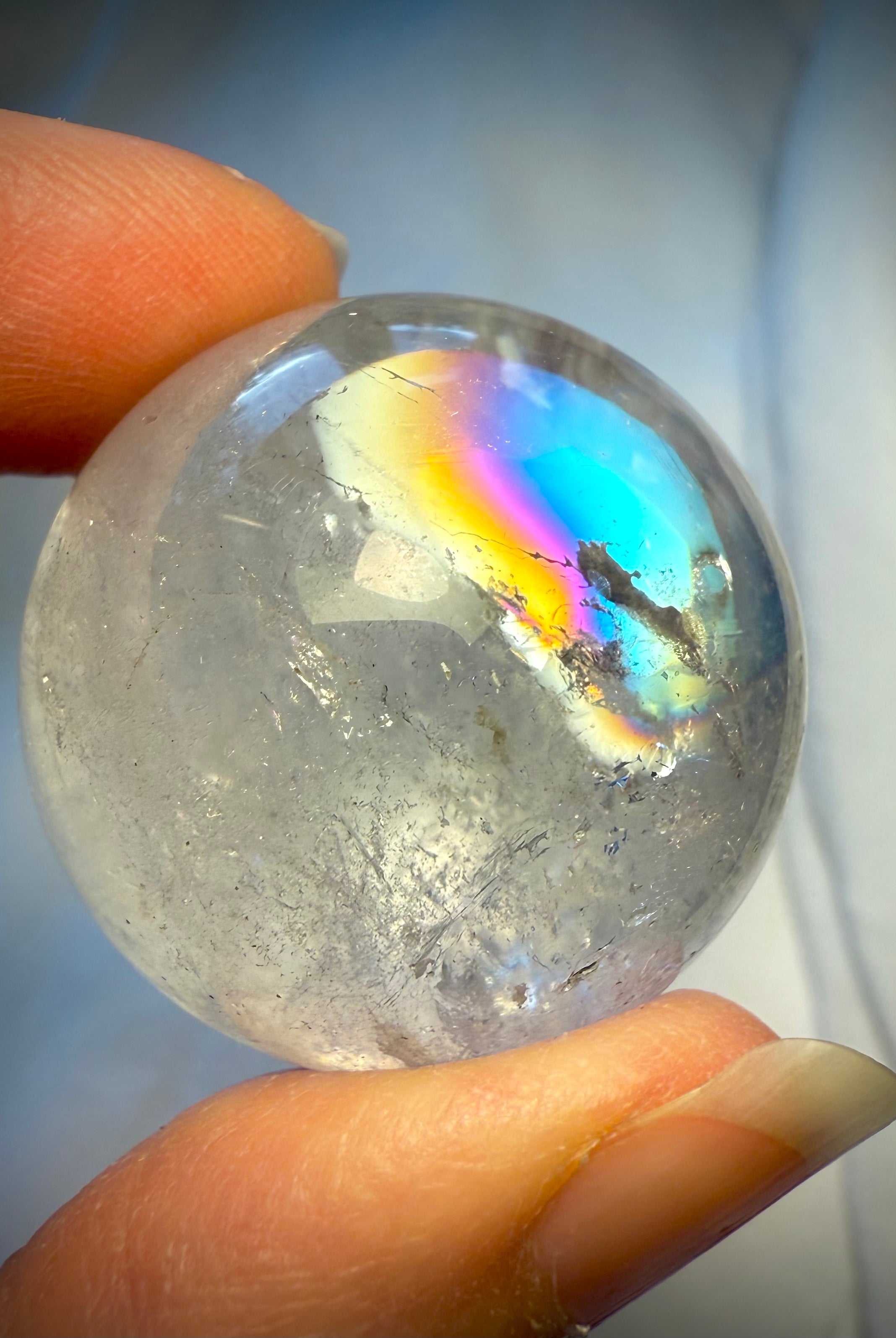 Stunning Rainbow Quartz sphere with intense prismatic flash held at fingertips – high-vibration crystal for crown chakra and lightwork
