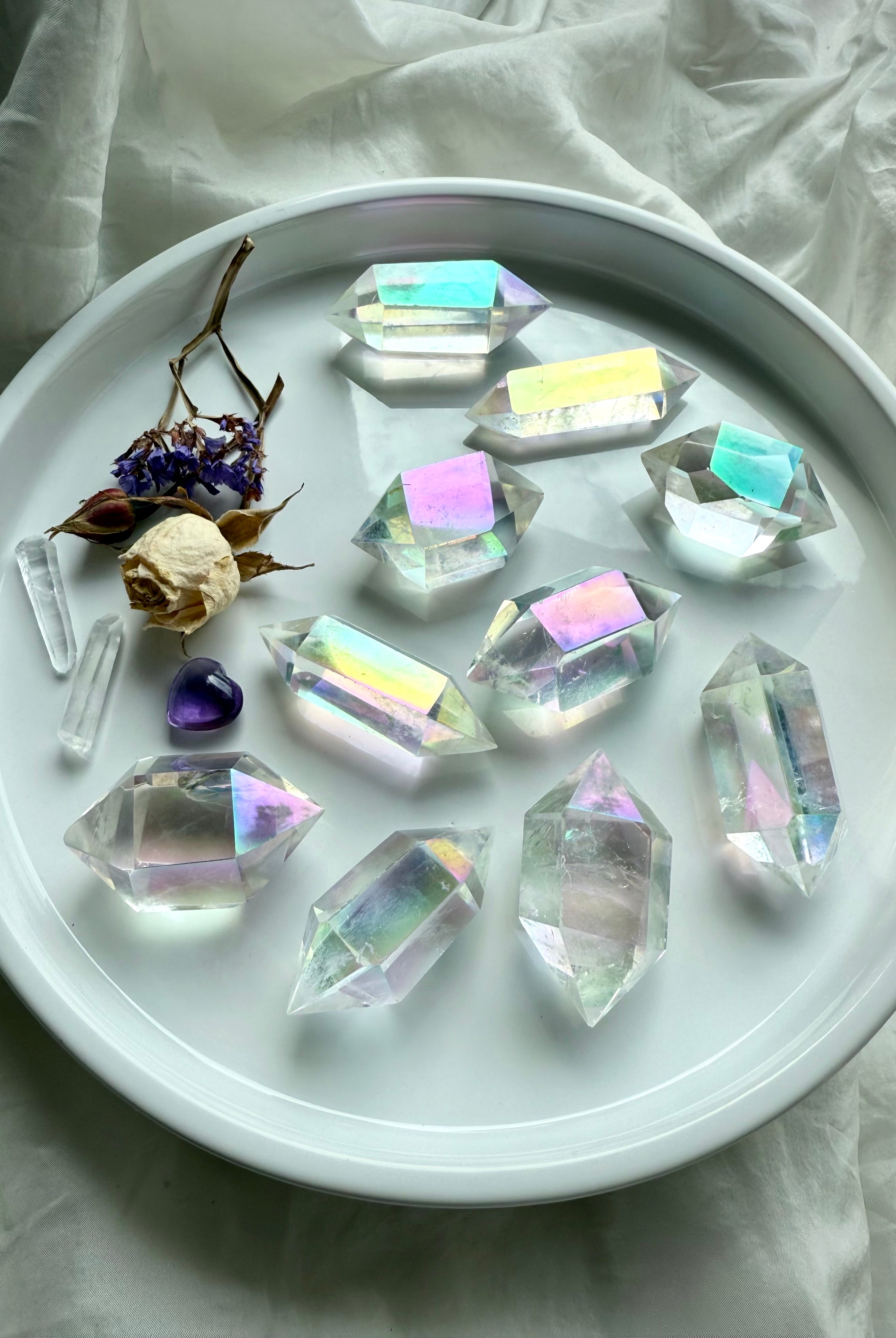 Angel Aura Quartz double terminated points with pastel rainbow glow displayed in a white dish for meditation and chakra healing