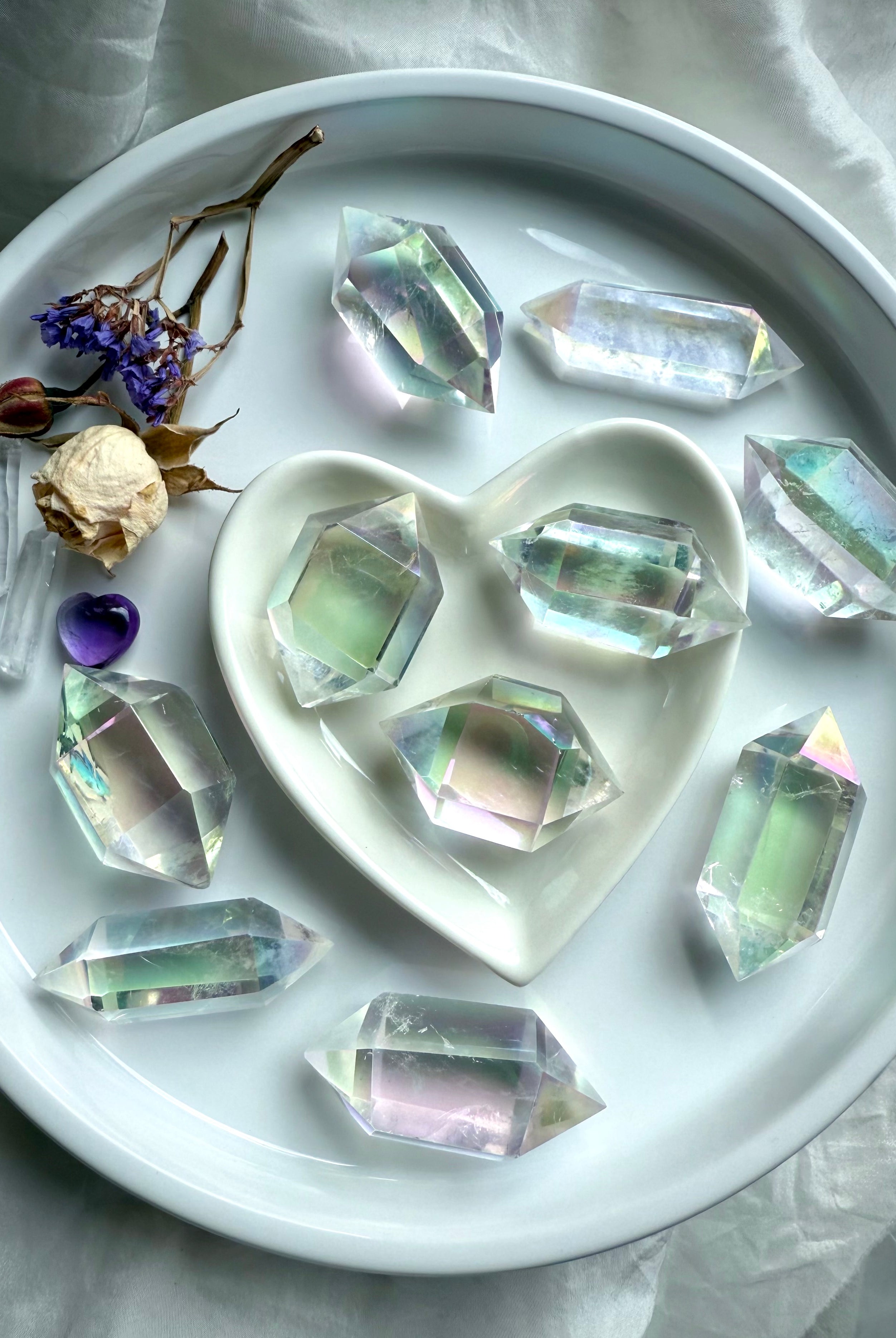 Iridescent Angel Aura Quartz double terminated crystal points in a round dish with heart-shaped bowl, rainbow sheen reflecting light