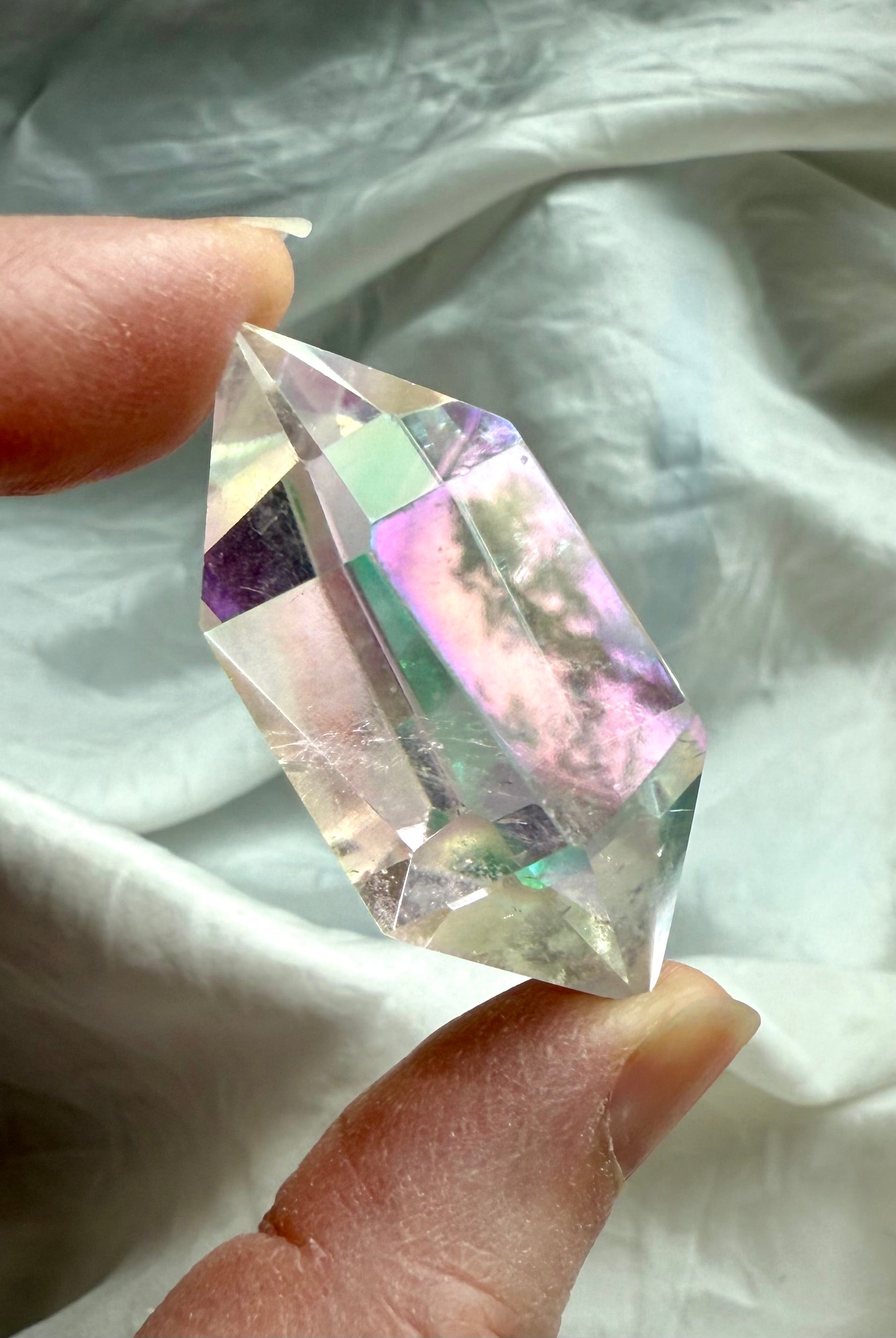 Closeup of clear Angel Aura Quartz DT crystal held in hand showing sharp double terminations and luminous rainbow aura coating