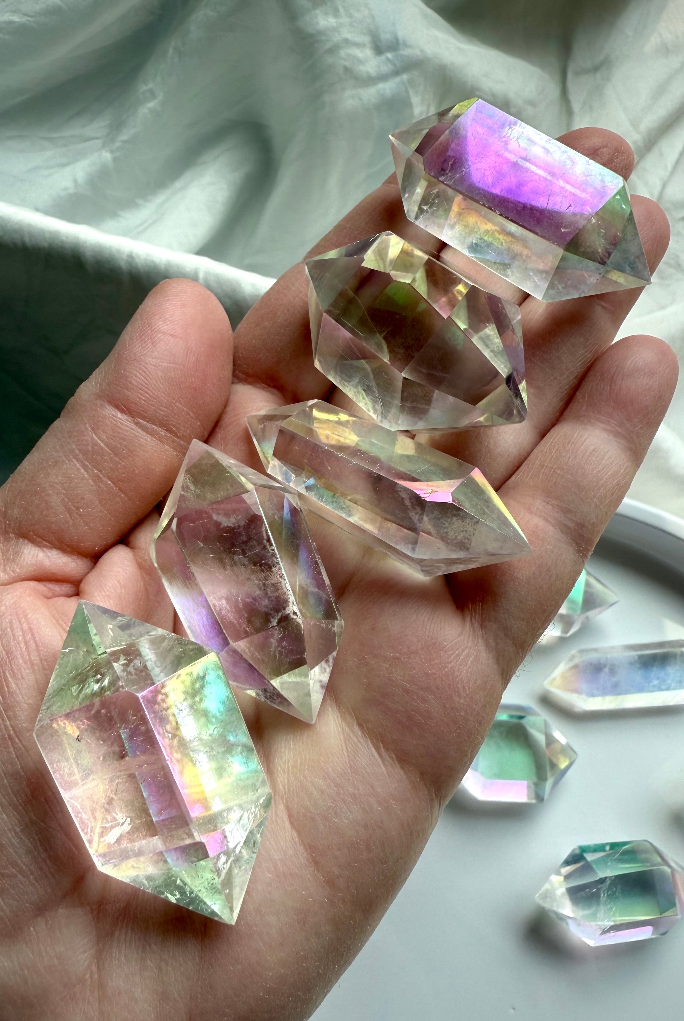 Hand holding several Angel Aura Quartz double terminated crystal points with rainbow sheen and faceted clarity