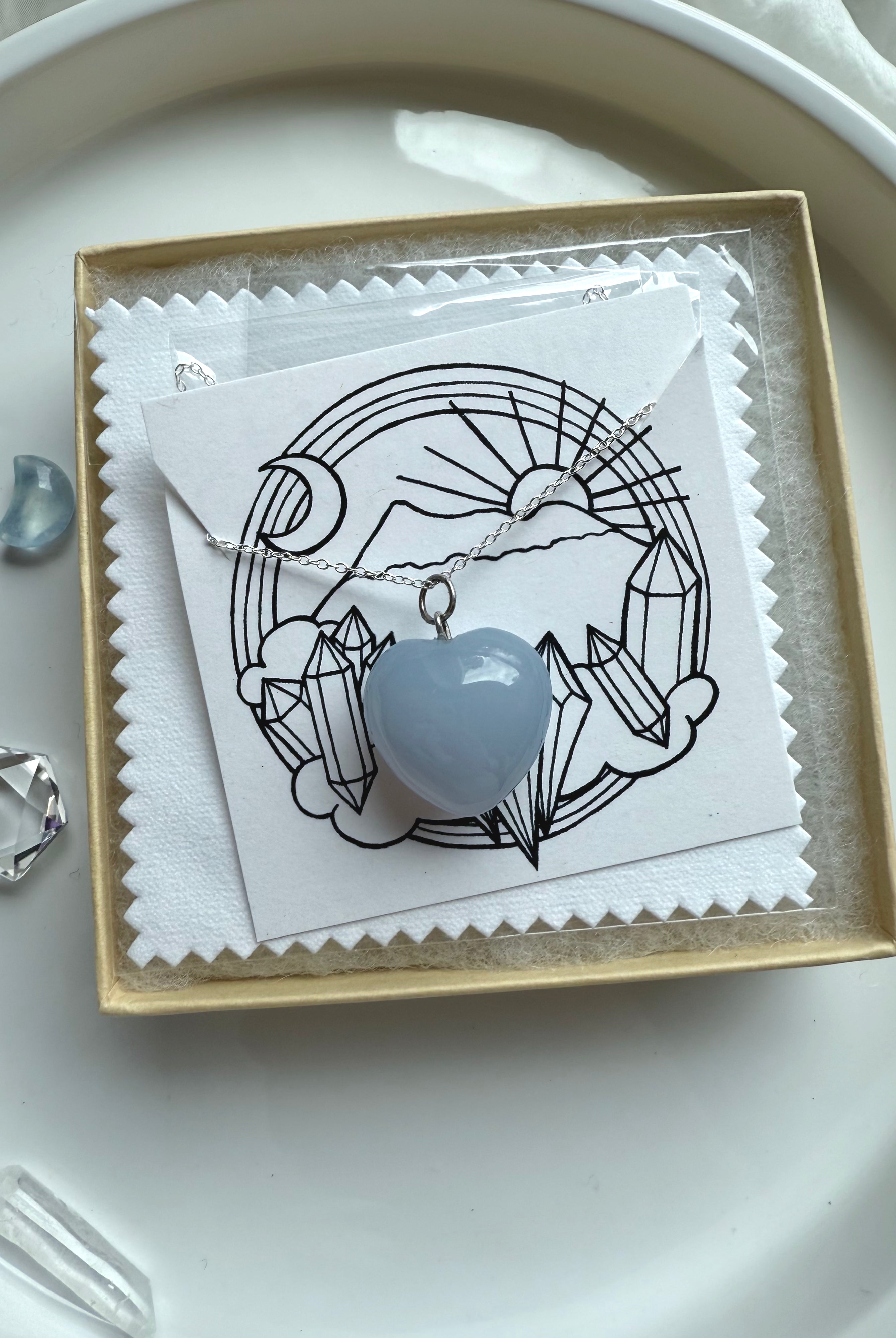 Blue Chalcedony heart necklace on silver chain, packaged with crystal-themed insert card and white polishing cloth.