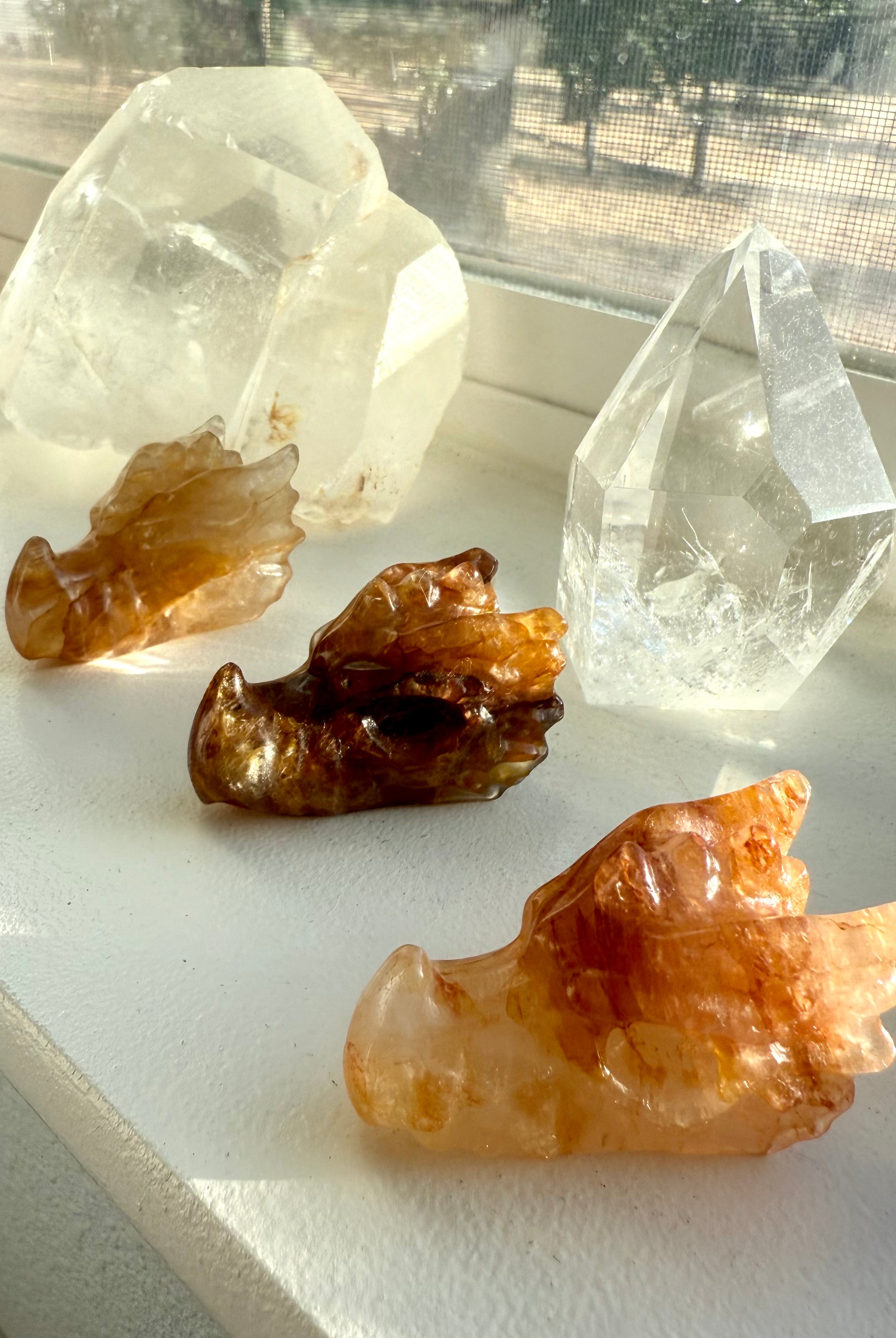 Golden Healer Quartz dragon head carvings with hematite inclusions displayed with clear quartz crystals — crystal dragon guardian for chakra healing.