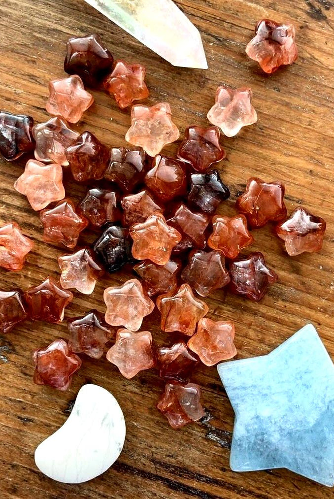 An array of vibrant red hematoid quartz mini crystal star carvings shown on a wood table