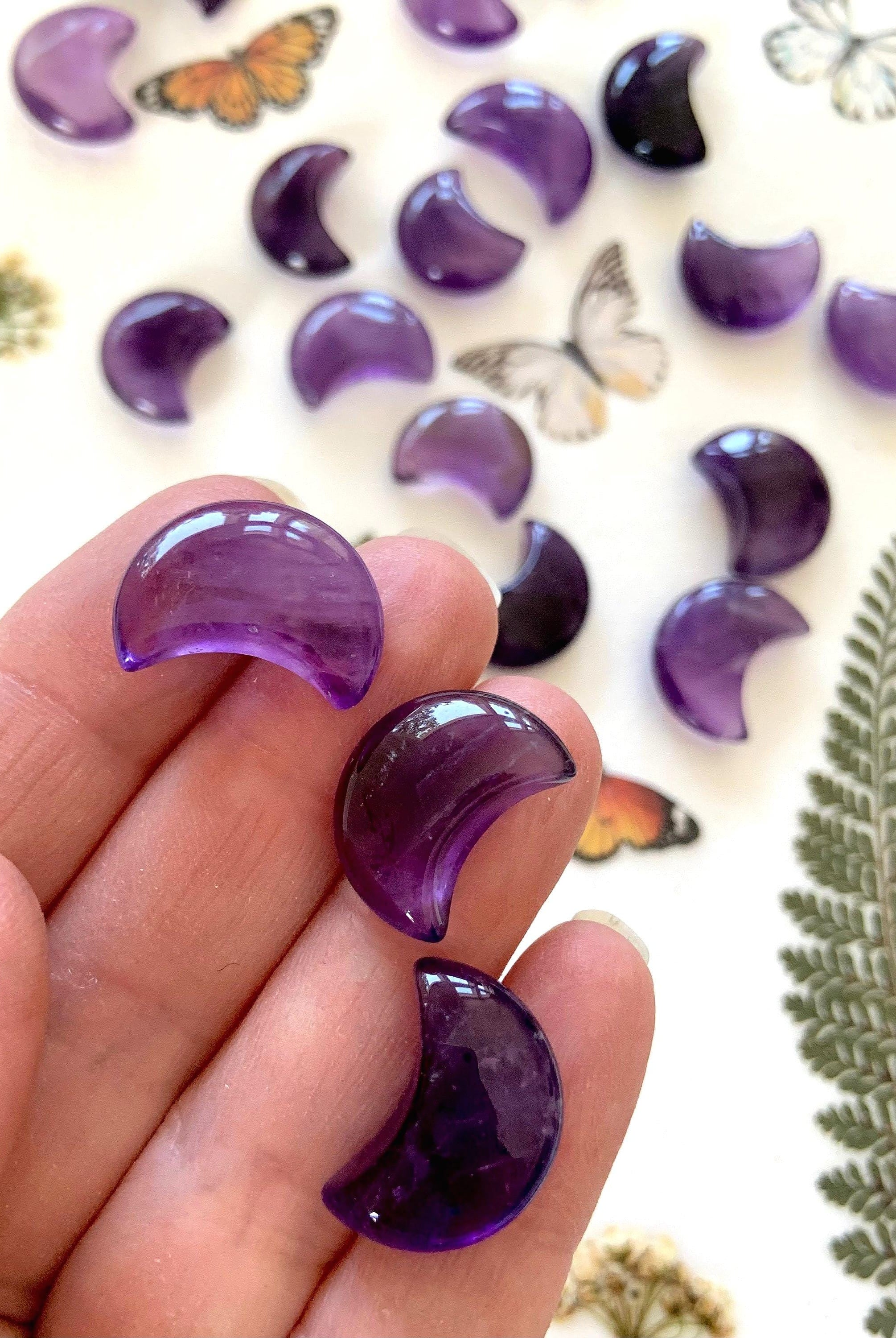 Mini sized purple amethyst moons shown on my hand with pretty crystals in the background