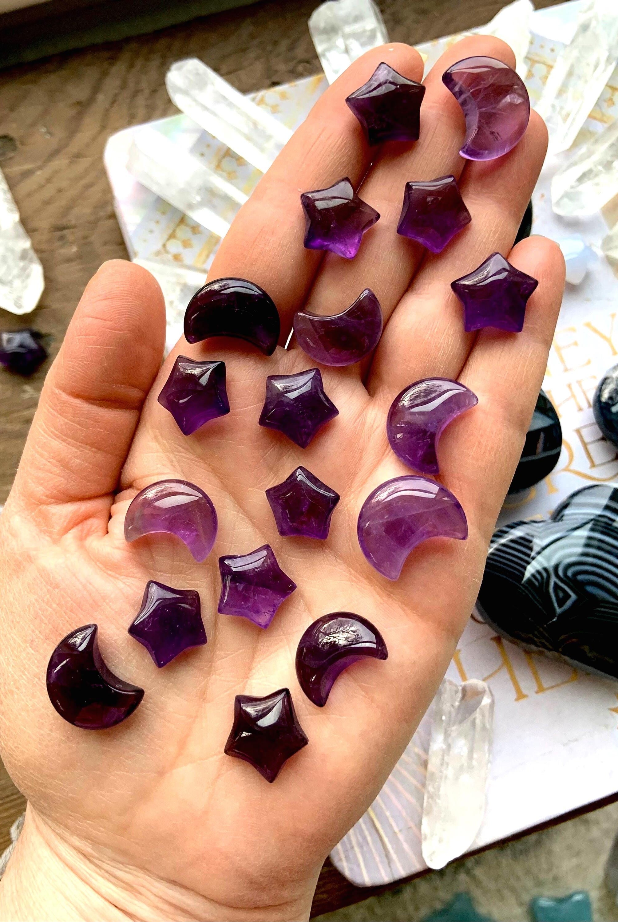 Mini sized purple amethyst moons and stars shown on my hand with pretty crystals in the background