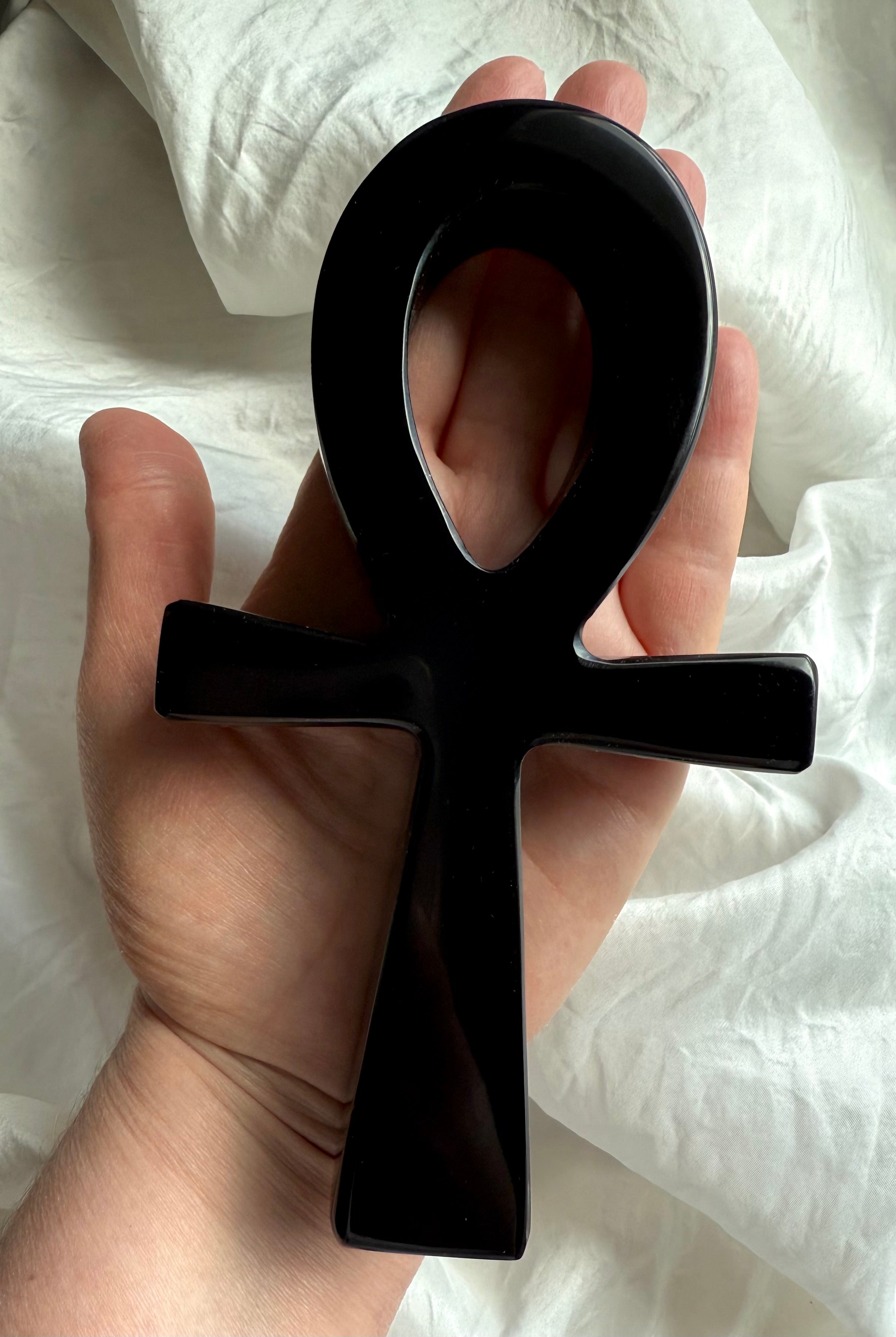 Polished black obsidian ankh carving resting in hand — sacred Egyptian life symbol crystal for grounding, protection, and meditation rituals.