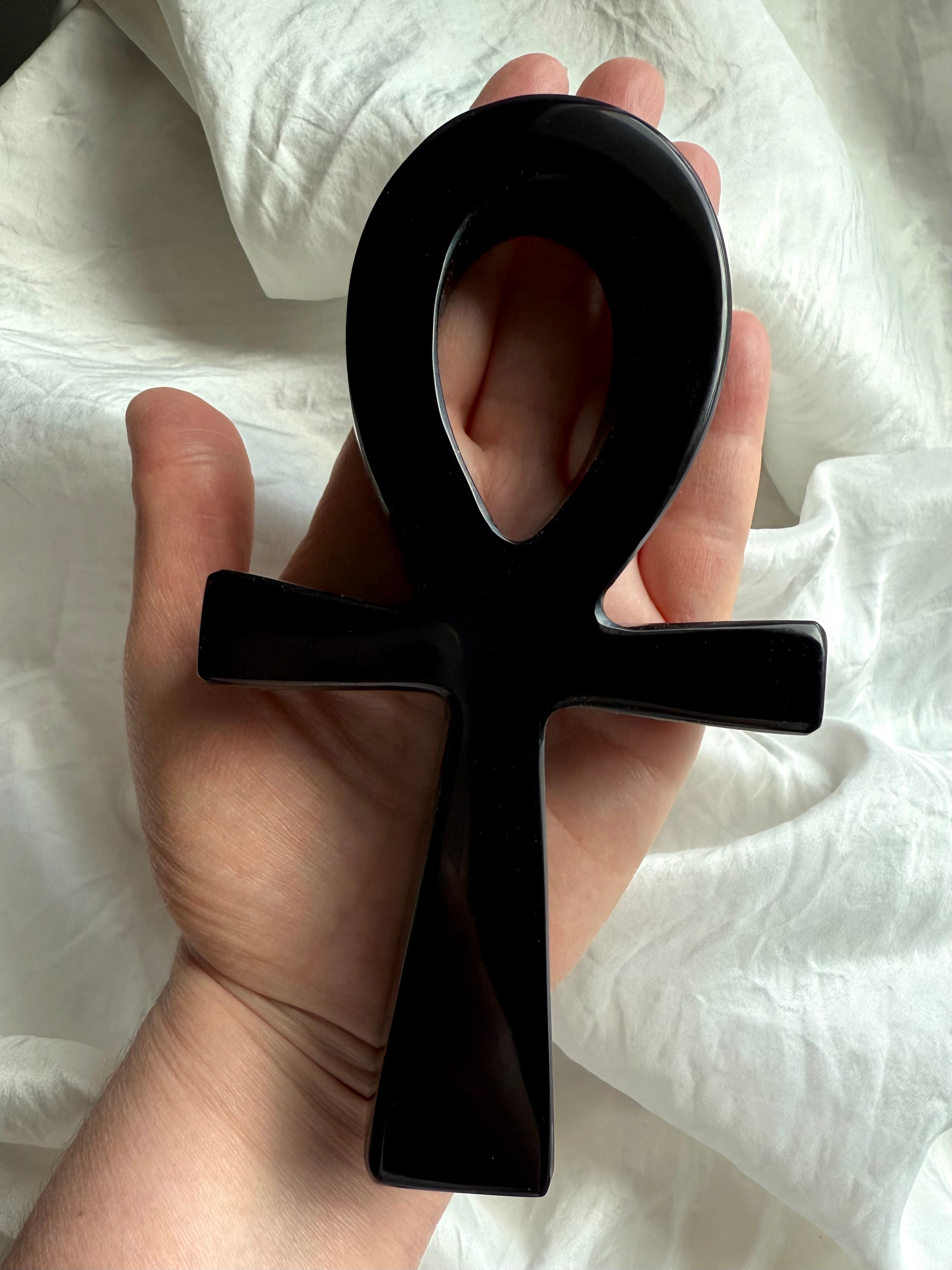 Polished black obsidian ankh carving resting in hand — sacred Egyptian life symbol crystal for grounding, protection, and meditation rituals.