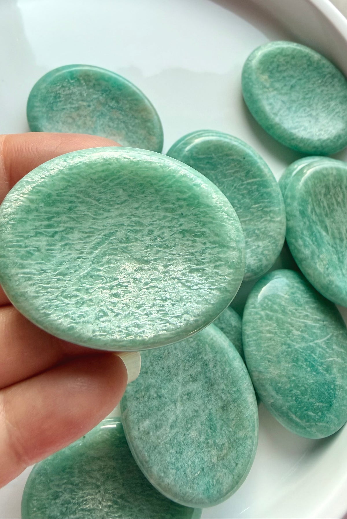 Natural Amazonite worry stone held between fingers, showing soft blue-green coloring, subtle white streaks and smooth polished surface