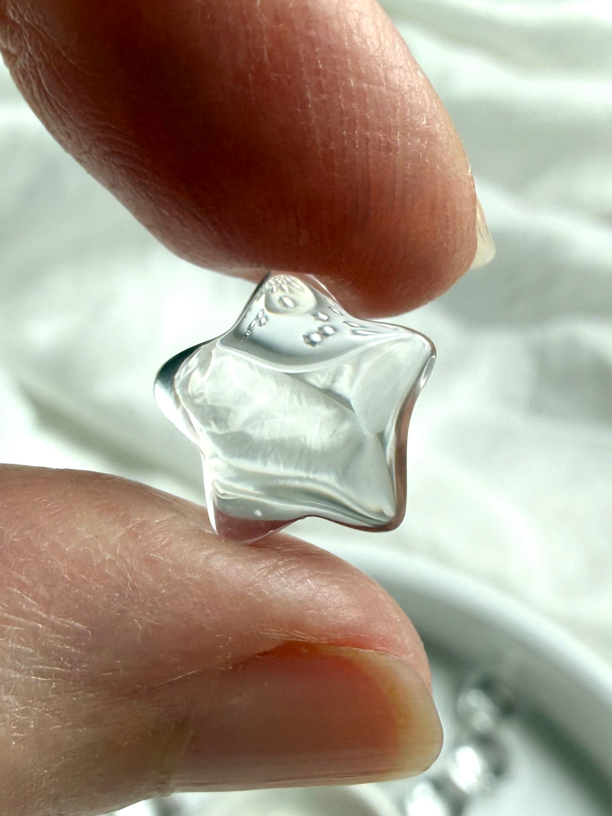 Tiny Clear Quartz star crystal held between fingers, showing natural transparency, polished facets and delicate five-point celestial shape