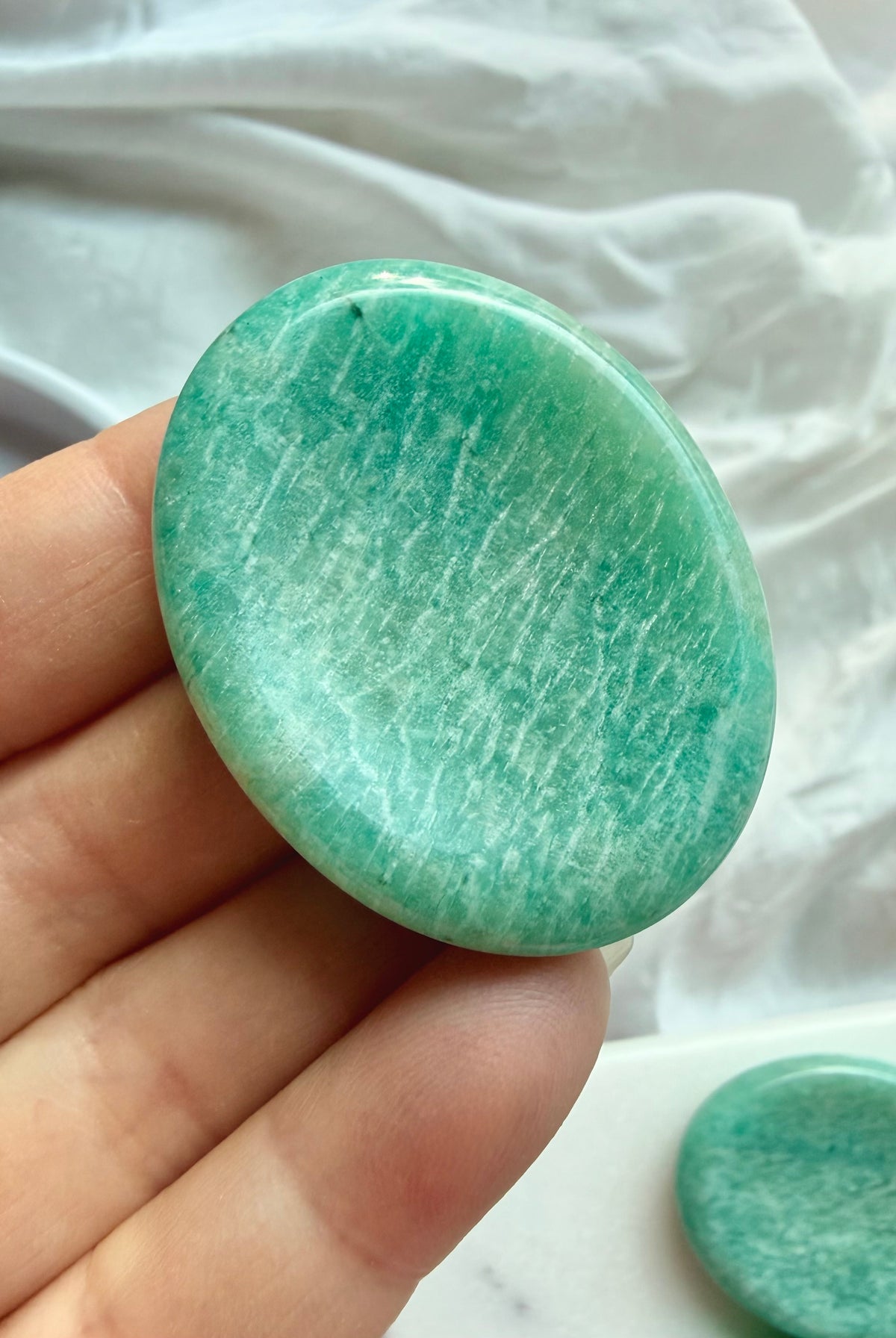 Natural Amazonite crystal worry stone held in hand, featuring beautiful seafoam-green tones and subtle white mineral inclusions