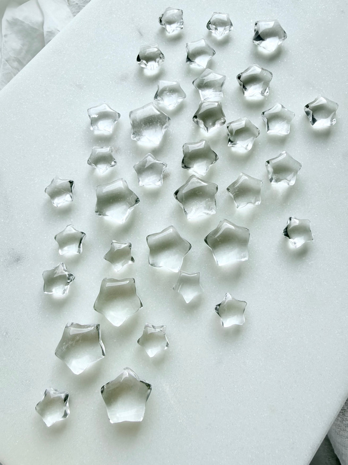 Tiny Clear Quartz star gemstones arranged on a white background, polished five-point crystal stars for crafting, meditation and energy healing