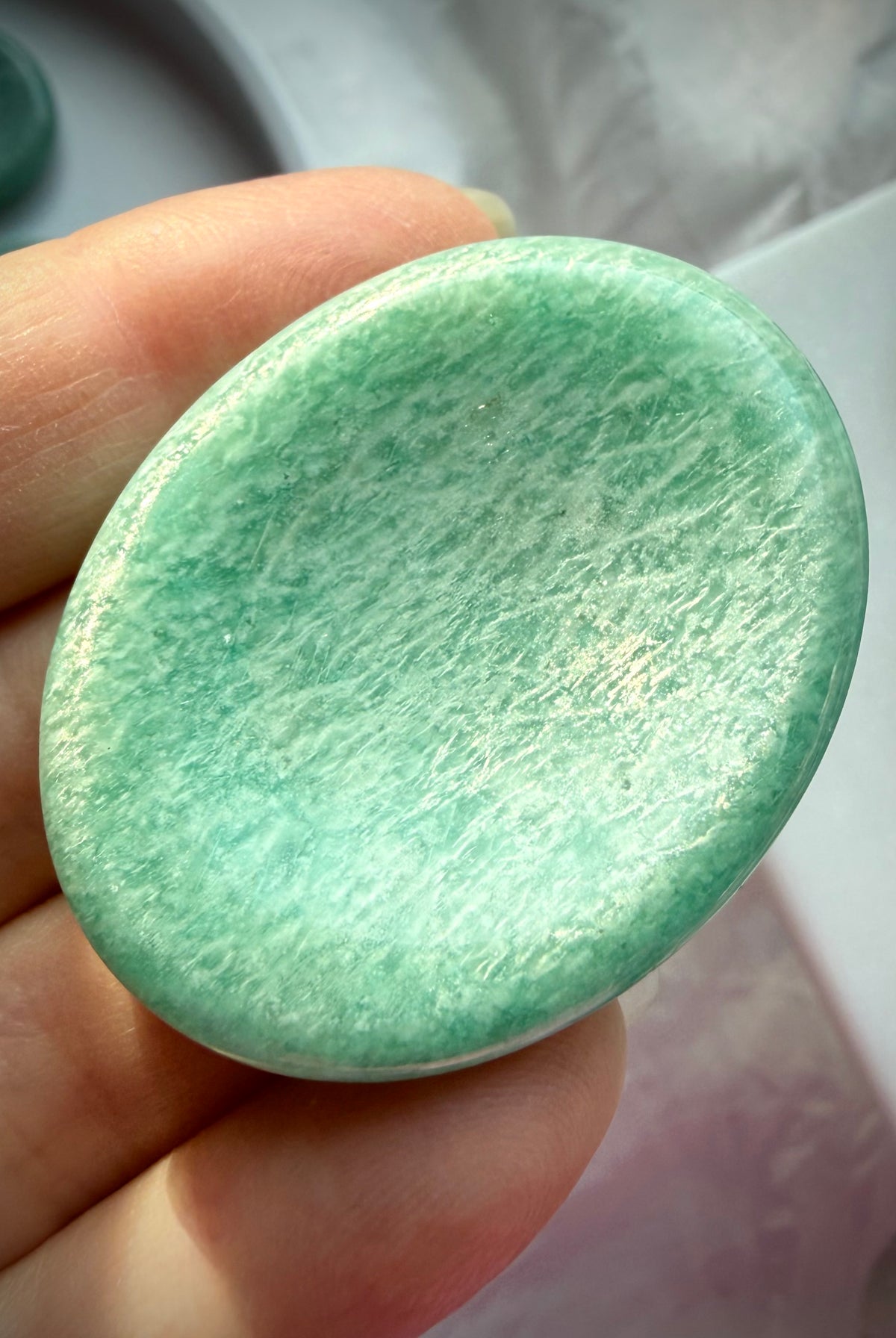 Amazonite thumb stone held between fingers, highlighting its glossy polish, natural white veining and soothing turquoise-green color