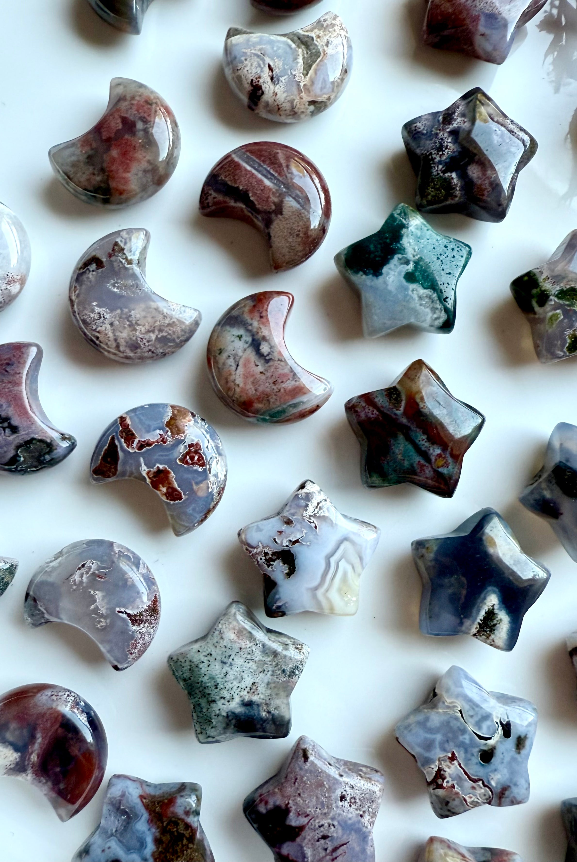 Assortment of Ocean Jasper moons and stars on a white tray — mini gemstone carvings in unique cosmic patterns for altar and crystal grids