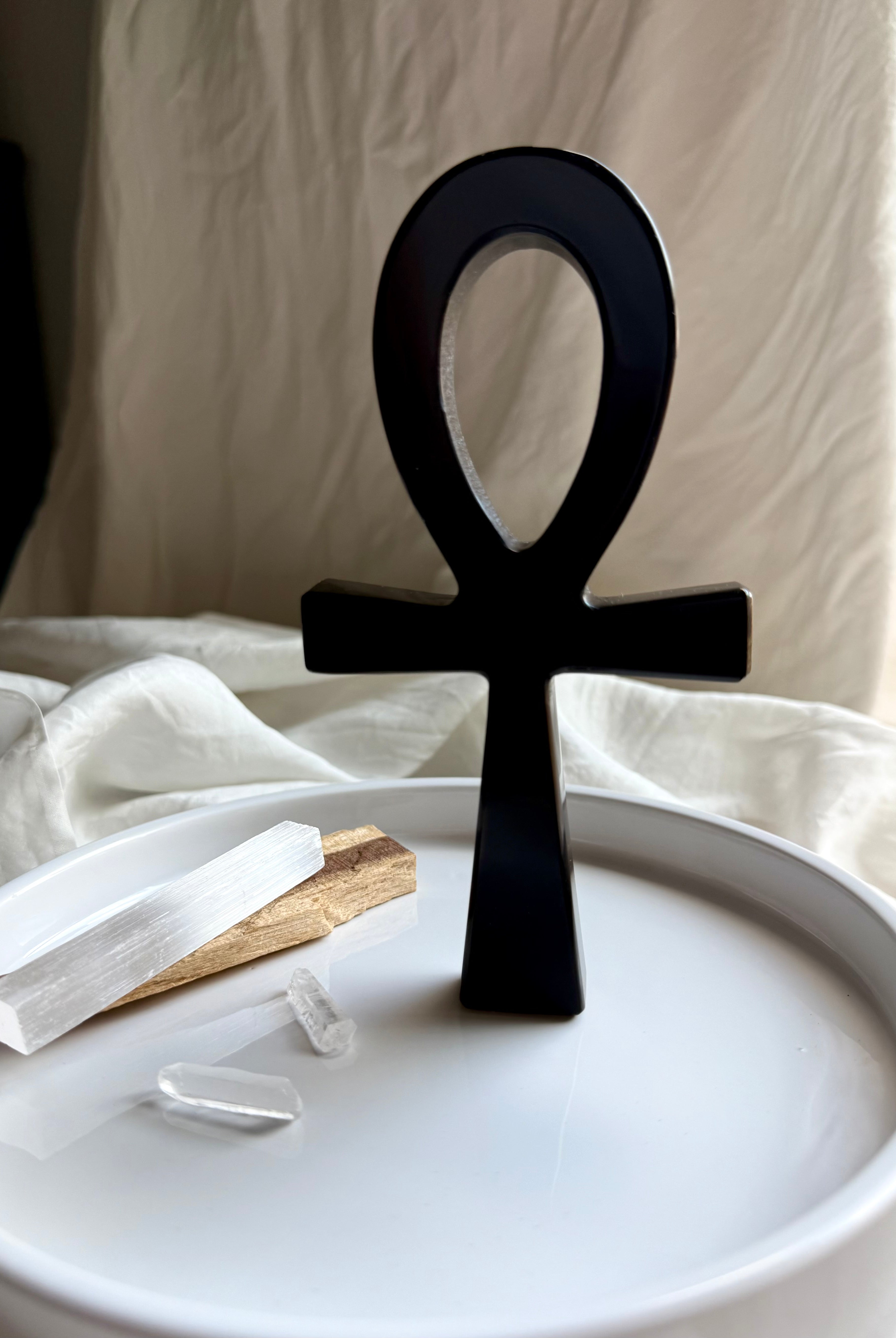 Standing Black obsidian ankh symbol on a white plate with palo santo and crystals