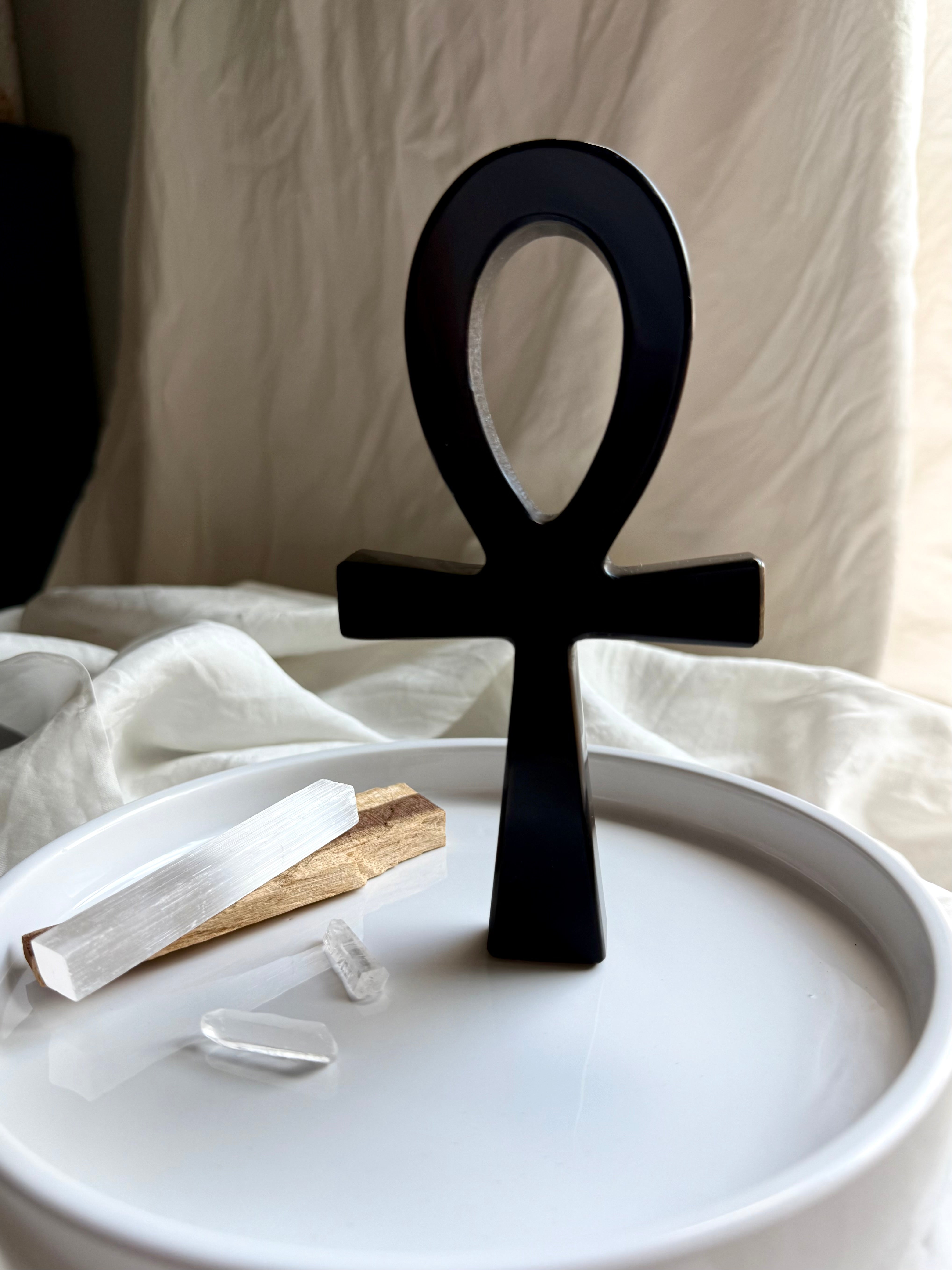 Standing Black obsidian ankh symbol on a white plate with palo santo and crystals