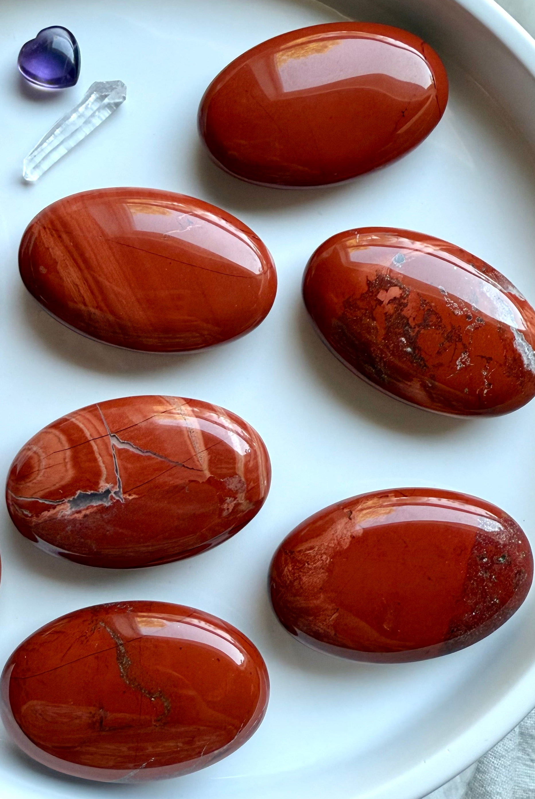 Brilliant Red Jasper palm stones on a white plate — grounding Root Chakra crystals for meditation, showing natural color and pattern variation.