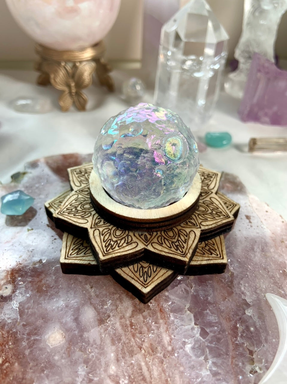 Angel Aura Full Moon crystal sphere on wood lotus stand atop a pink amethyst slab, surrounded by dreamy celestial crystals — radiant display decor.