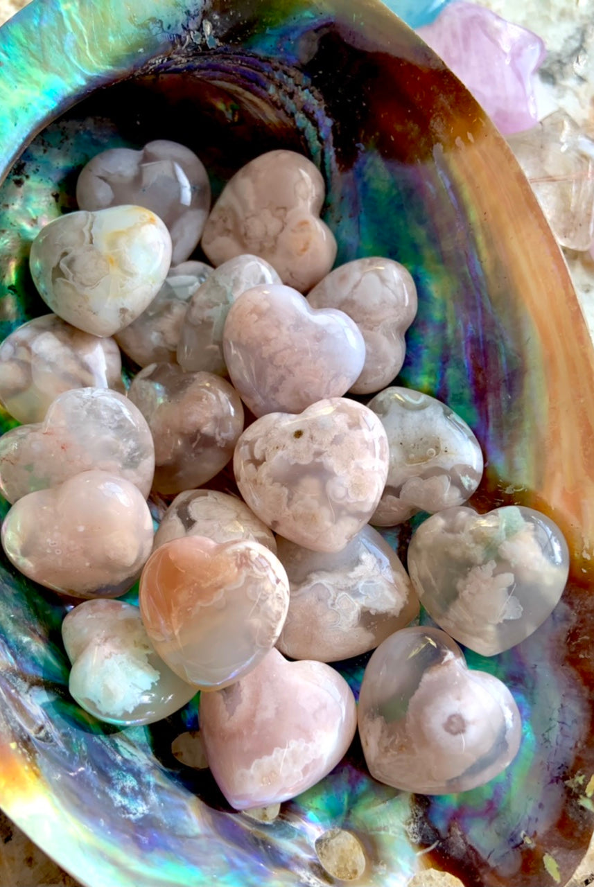 A colorful array of mini flower agate heart shapes inside an abalone shell