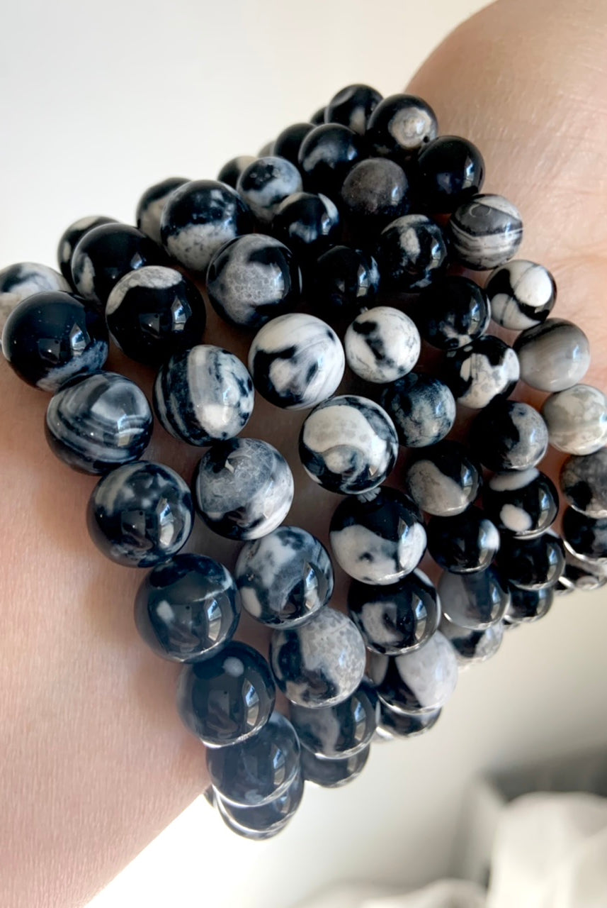 Side view of multiple Orca Agate bracelets stacked on wrist, showing bold black-and-white banded patterns with subtle gray marbling in polished round beads