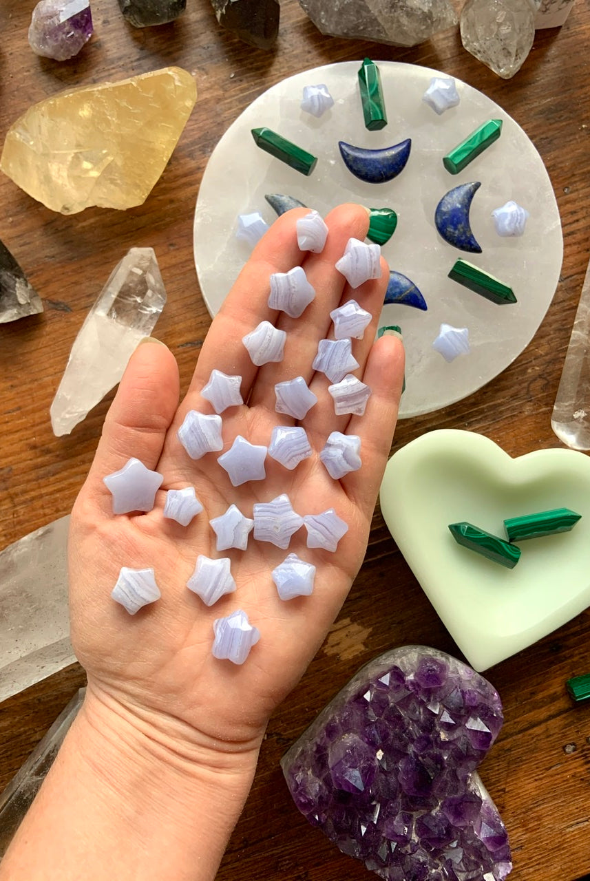 Blue Lace Agate stars on a hand, shown with a crystal grid & assorted crystals on a wood table — tools for peaceful, intentional energy work
