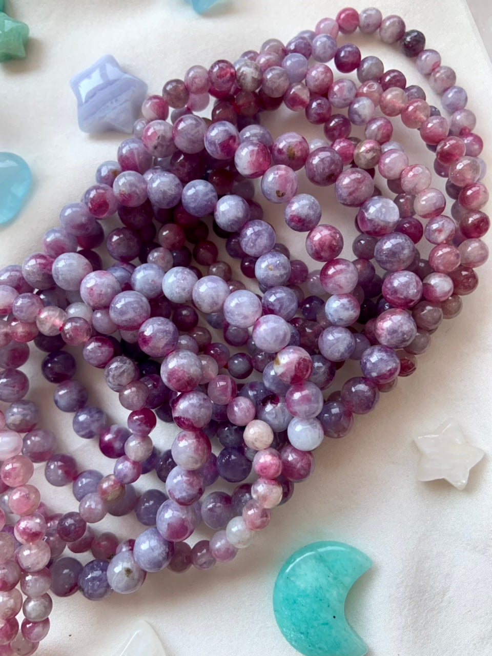 Array of Unicorn Stone crystal bracelets on white silk surrounded by celestial crystals — soothing energy tools for emotional healing + spiritual calm.